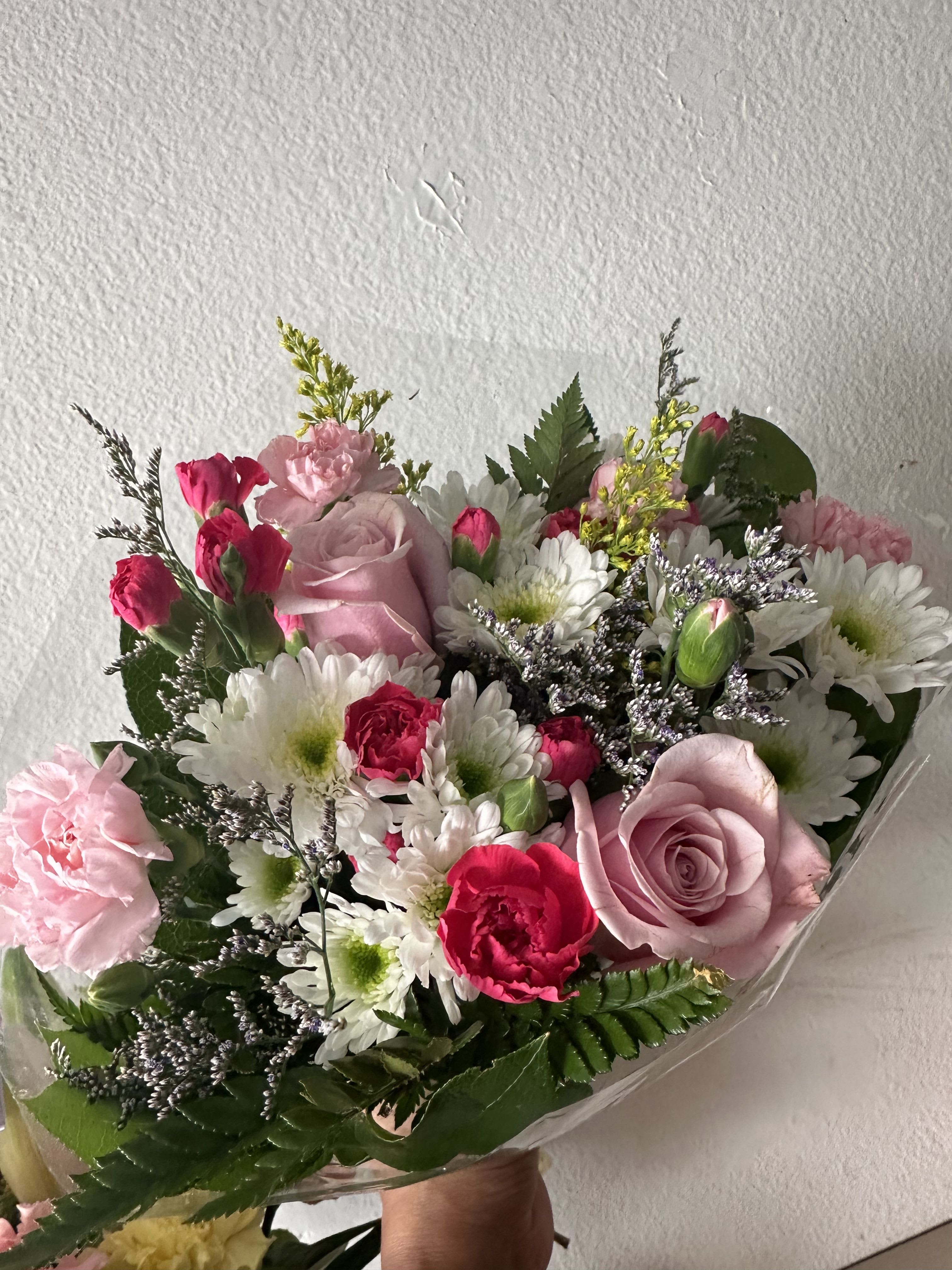 Bouquet of pink roses, carnations, and white daisies wrapped in clear plastic