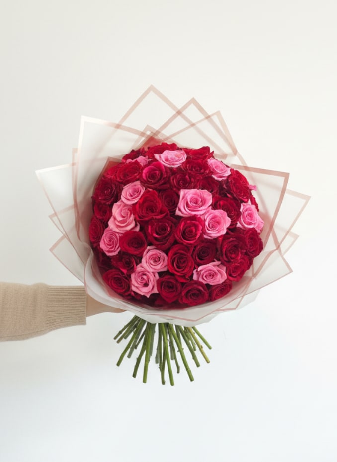 Young Mama - A dense, dome-shaped hand-tied bouquet of saturated red and soft pink roses that reads instantly as a romantic, celebratory Mother's Day bouquet for the young moms at heart in your life. The striking mix of deep red and blushing pink roses - with hints of white in the palette - creates a warm, affectionate message: she'll feel cherished and celebrated the moment she sees it.  Tightly packed into a compact, rounded cluster, each lush rose head forms a plush, tactile surface that begs to be admired. Clear floral wrap gives the bouquet a clean, modern outline while keeping the focus on color and texture; long stems are gathered neatly below for a polished hand-tied look that's easy to carry. Ideal for anniversaries, Valentine's Day, or most importantly this Mother's Day for young mothers, it's the kind of bouquet that says "you're seen" without needing words.  Send it as a meaningful surprise for the young mom you're thinking of - she'll feel truly adored. Order for same-day delivery when available; keep roses in fresh water and out of direct sunlight to help blooms last.