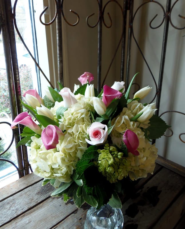 Pink calla lilies and white tulips arranged with pale hydrangeas in a glass vase.