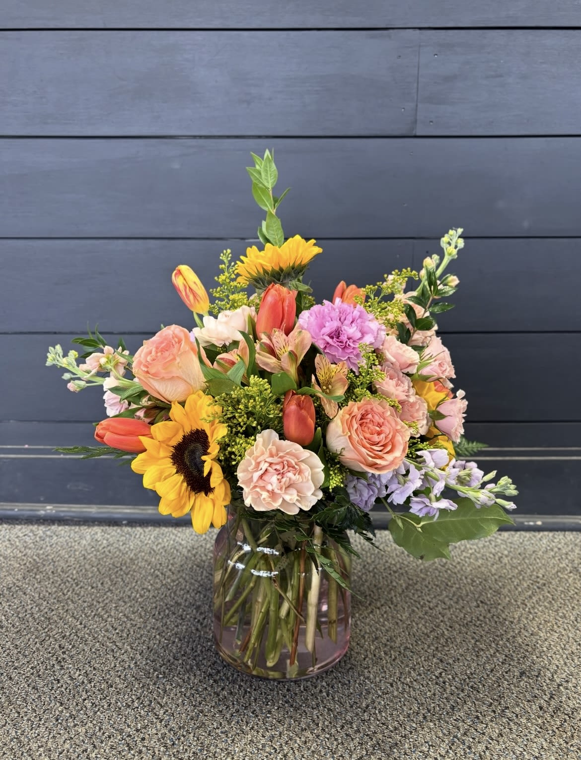 Wild Child - This tall pink cinched vase is filled with beautiful blooms of roses, sunflowers, carnations and so much more 
