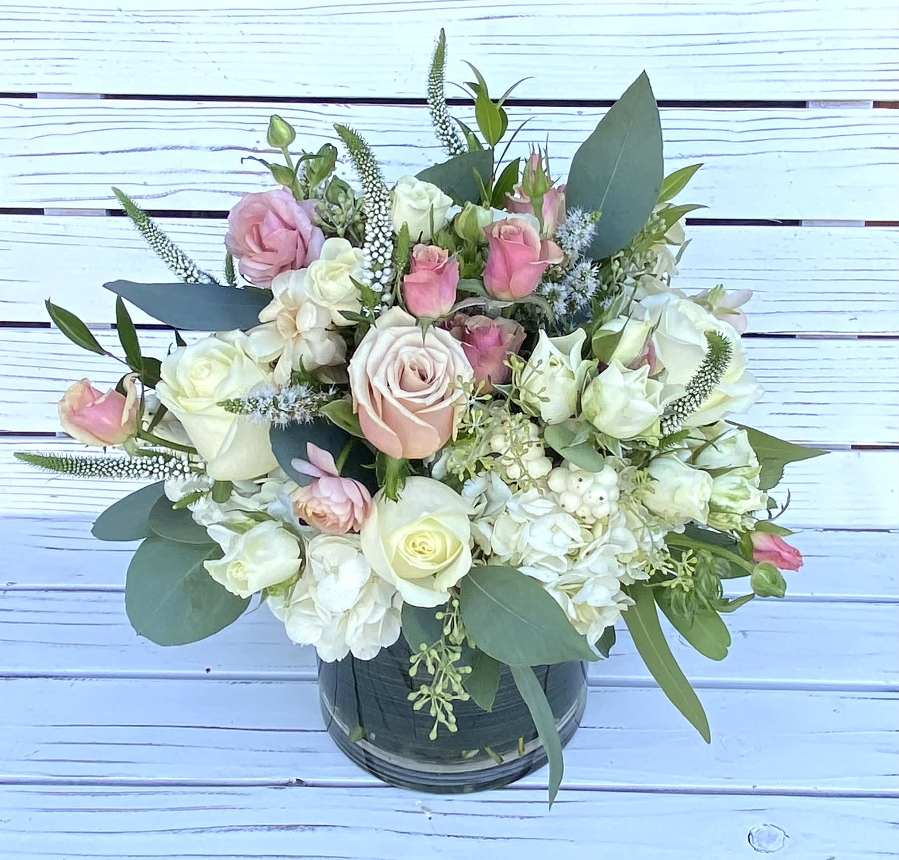 Low arrangement of white and blush roses and hydrangeas in a clear glass cylinder vase