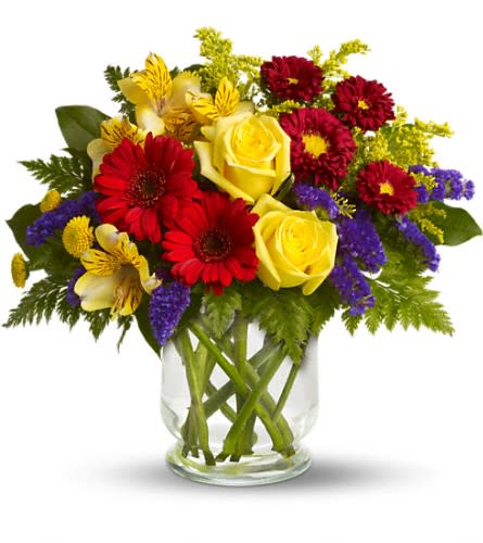Mixed bouquet of yellow roses, red daisies, and purple filler in a glass vase