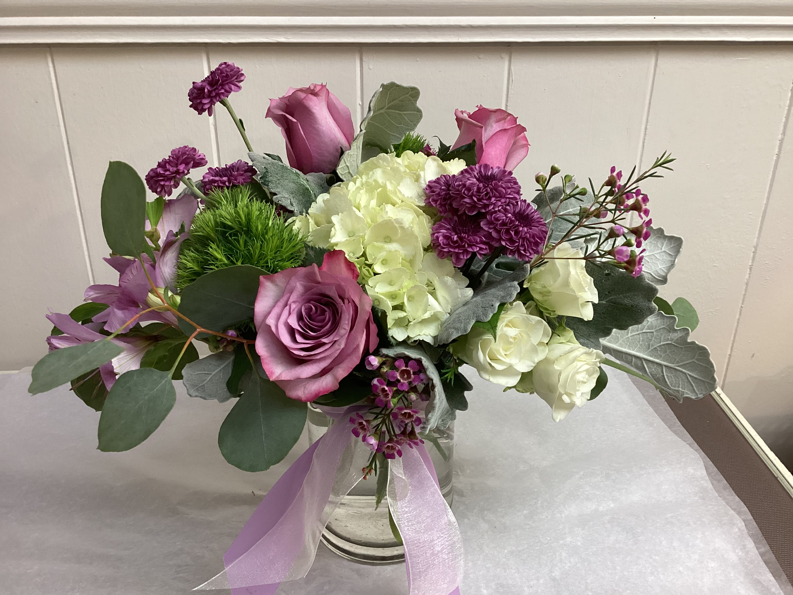 Pink and white floral arrangement in a clear glass vase with a lavender ribbon