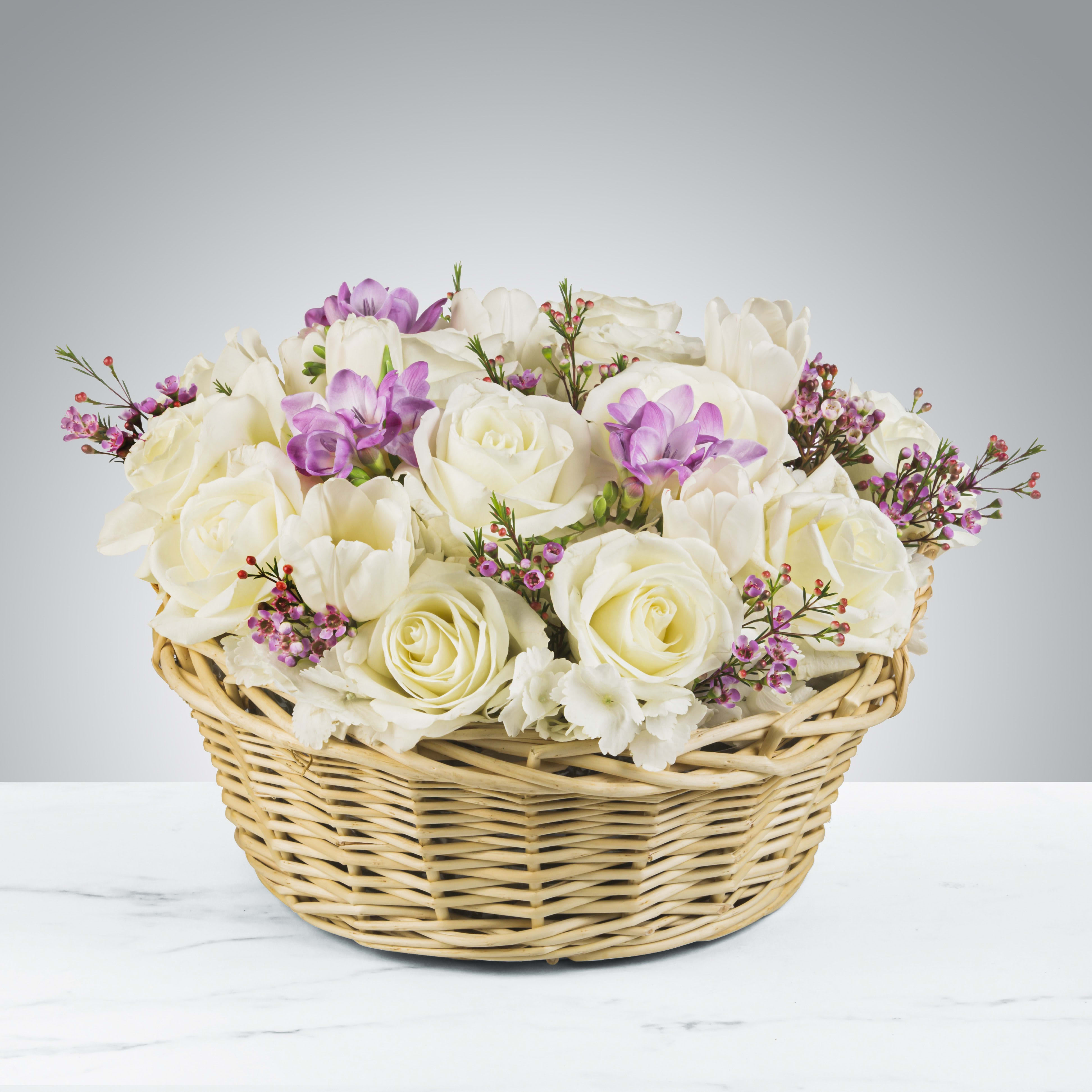 White roses and purple flowers arranged in a wicker basket
