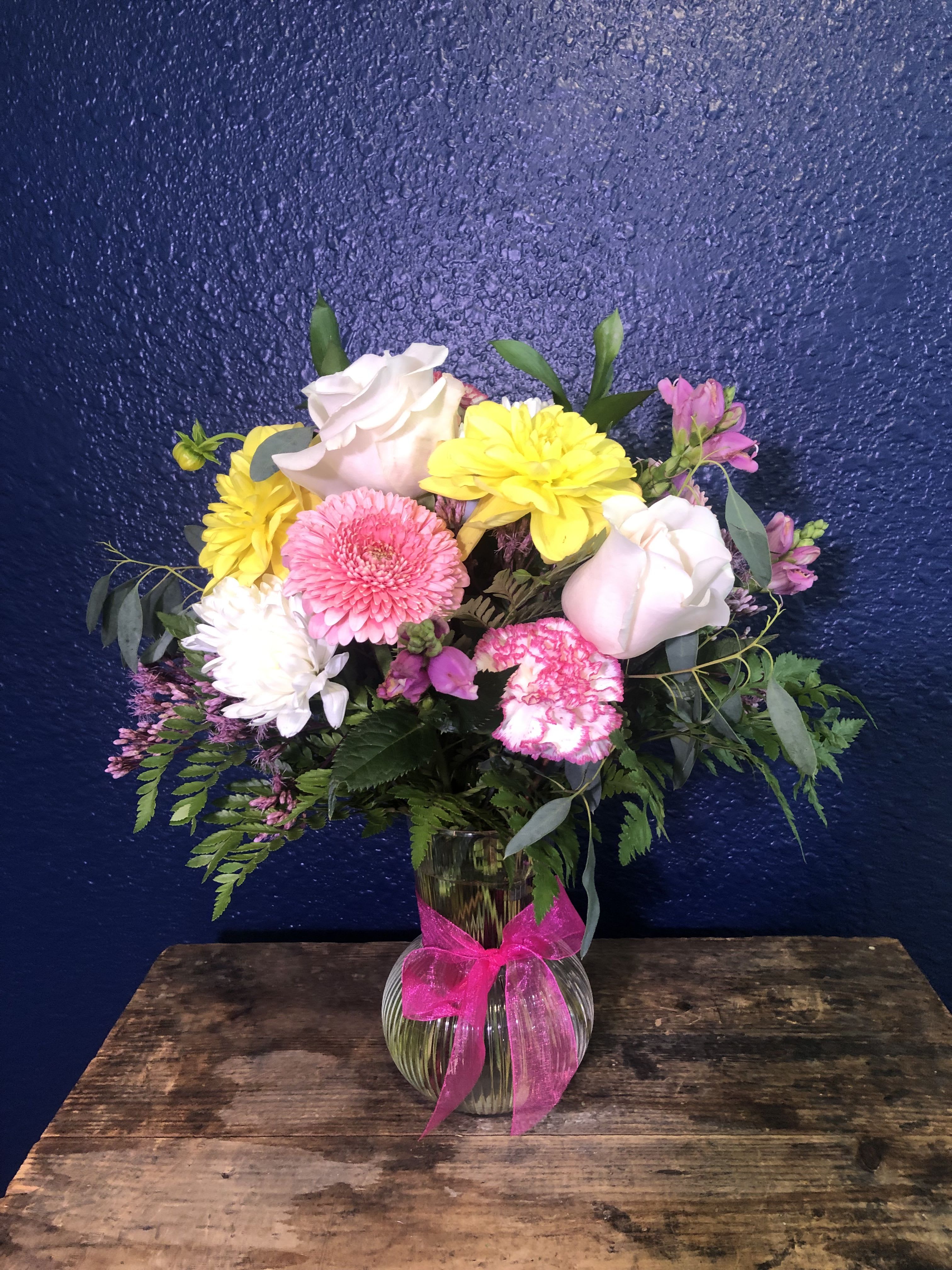 Mixed pink, yellow, and white flowers in a glass vase with a pink ribbon.
