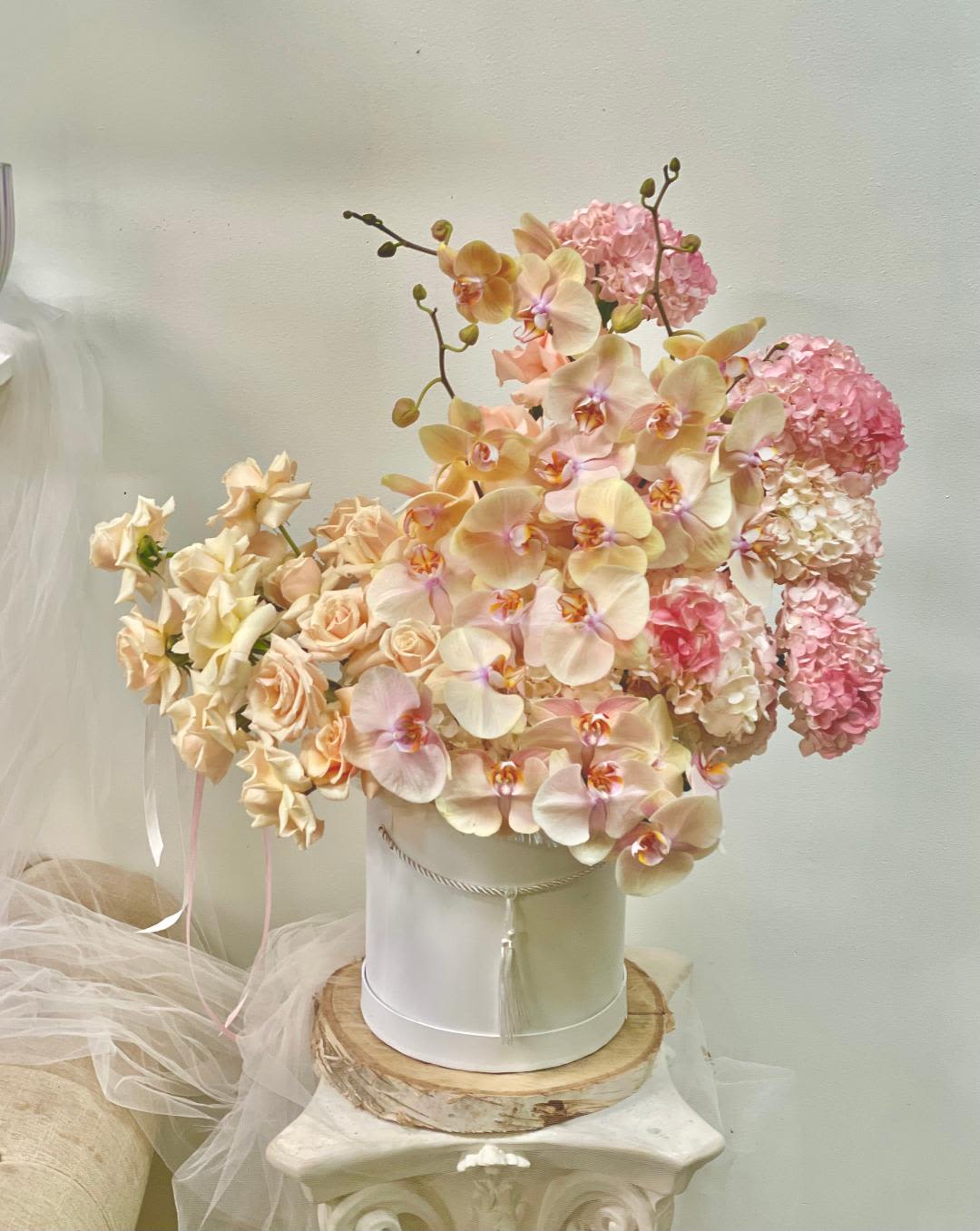 Peach orchids and pink hydrangeas arranged in a white hatbox