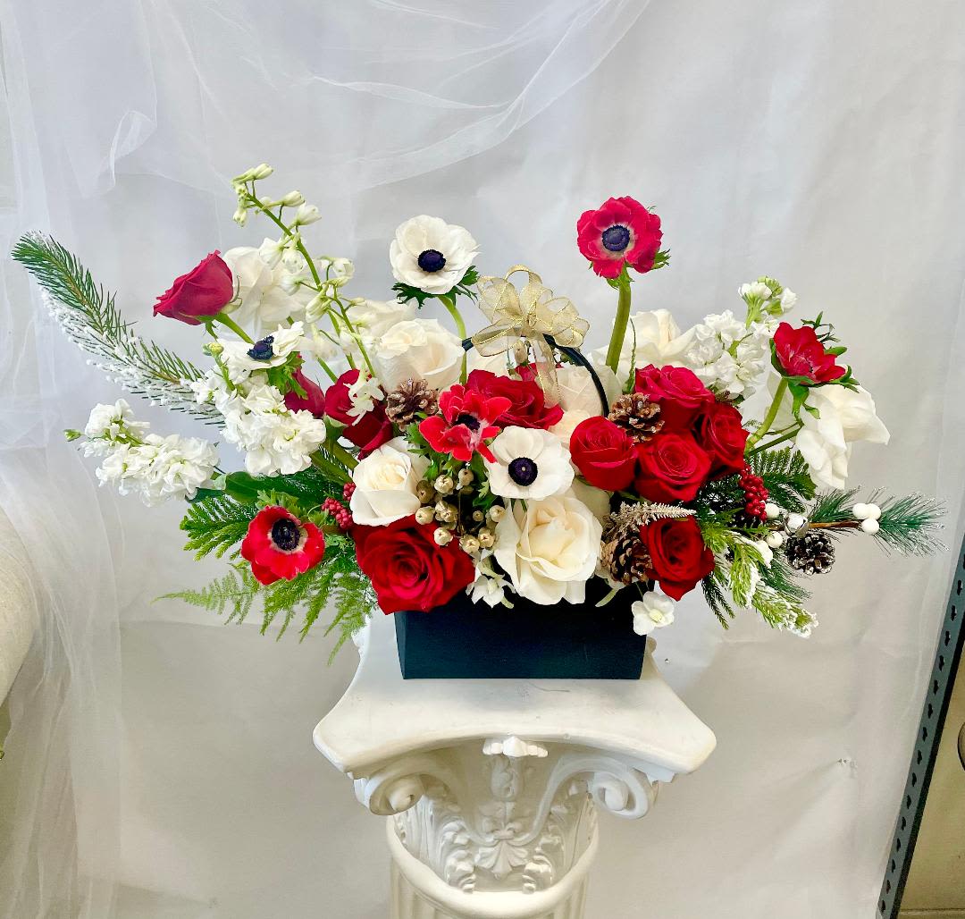Red and white floral arrangement in a black box with a gold ribbon