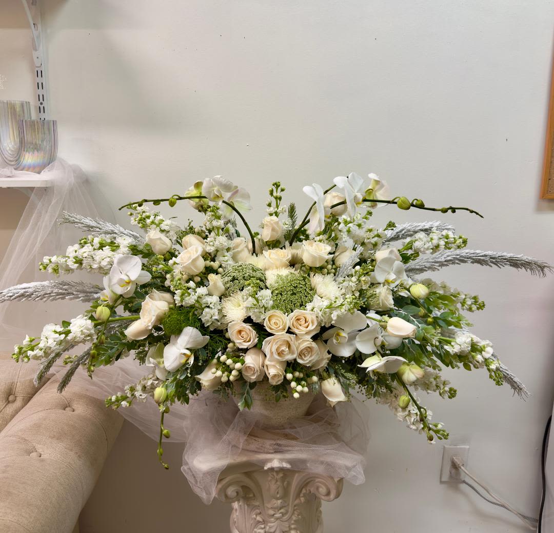 Large white floral arrangement with roses and orchids in a pedestal vase