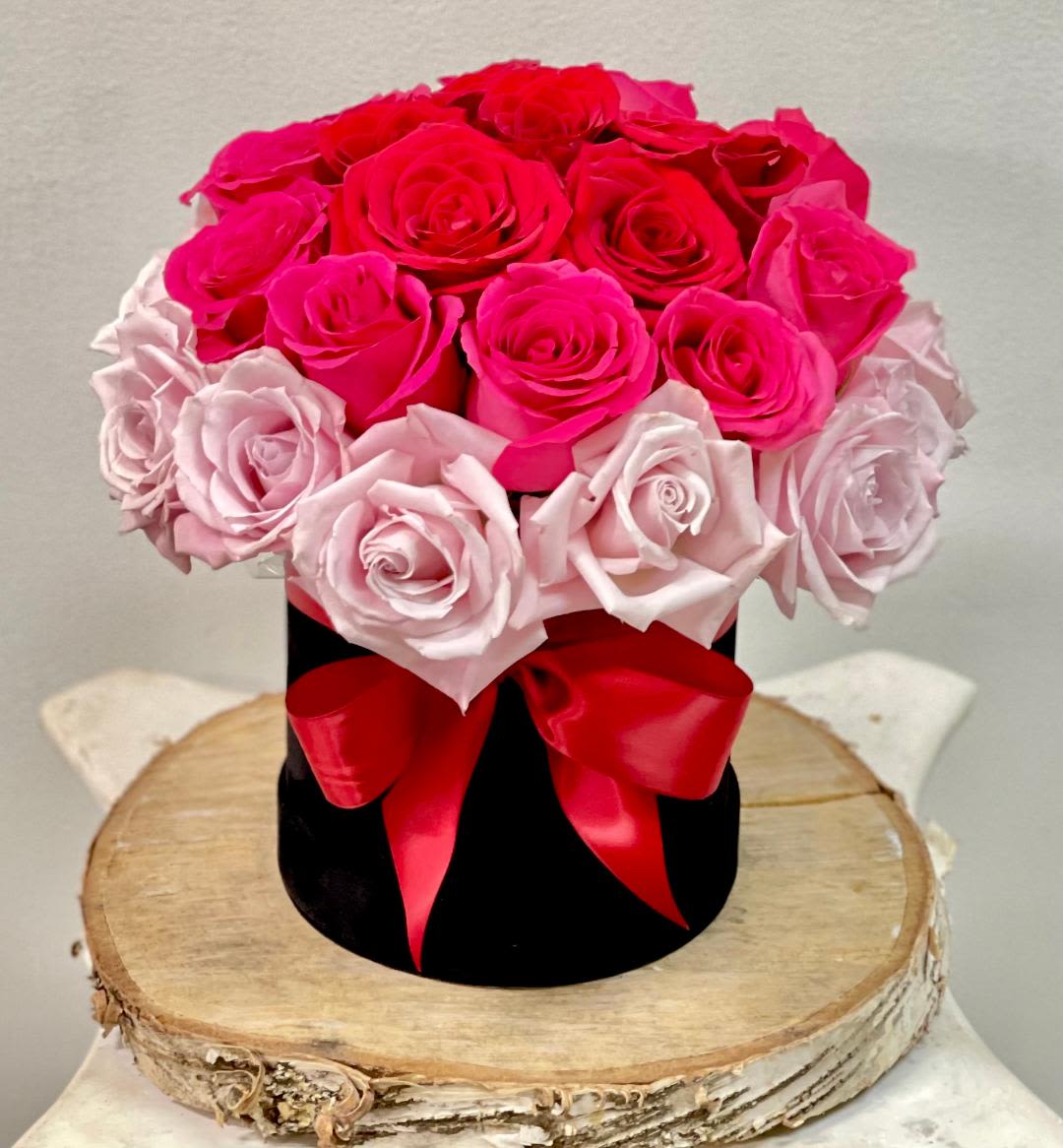 Pink and red roses arranged in a black hat box with a red ribbon