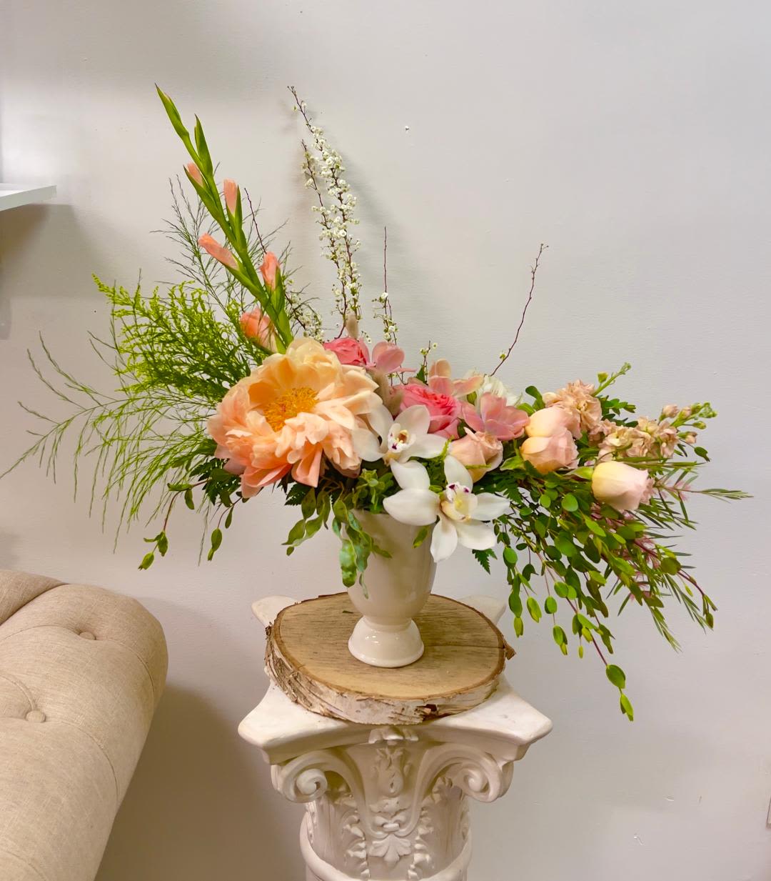 Peach and pink floral arrangement in a white vase on a pedestal