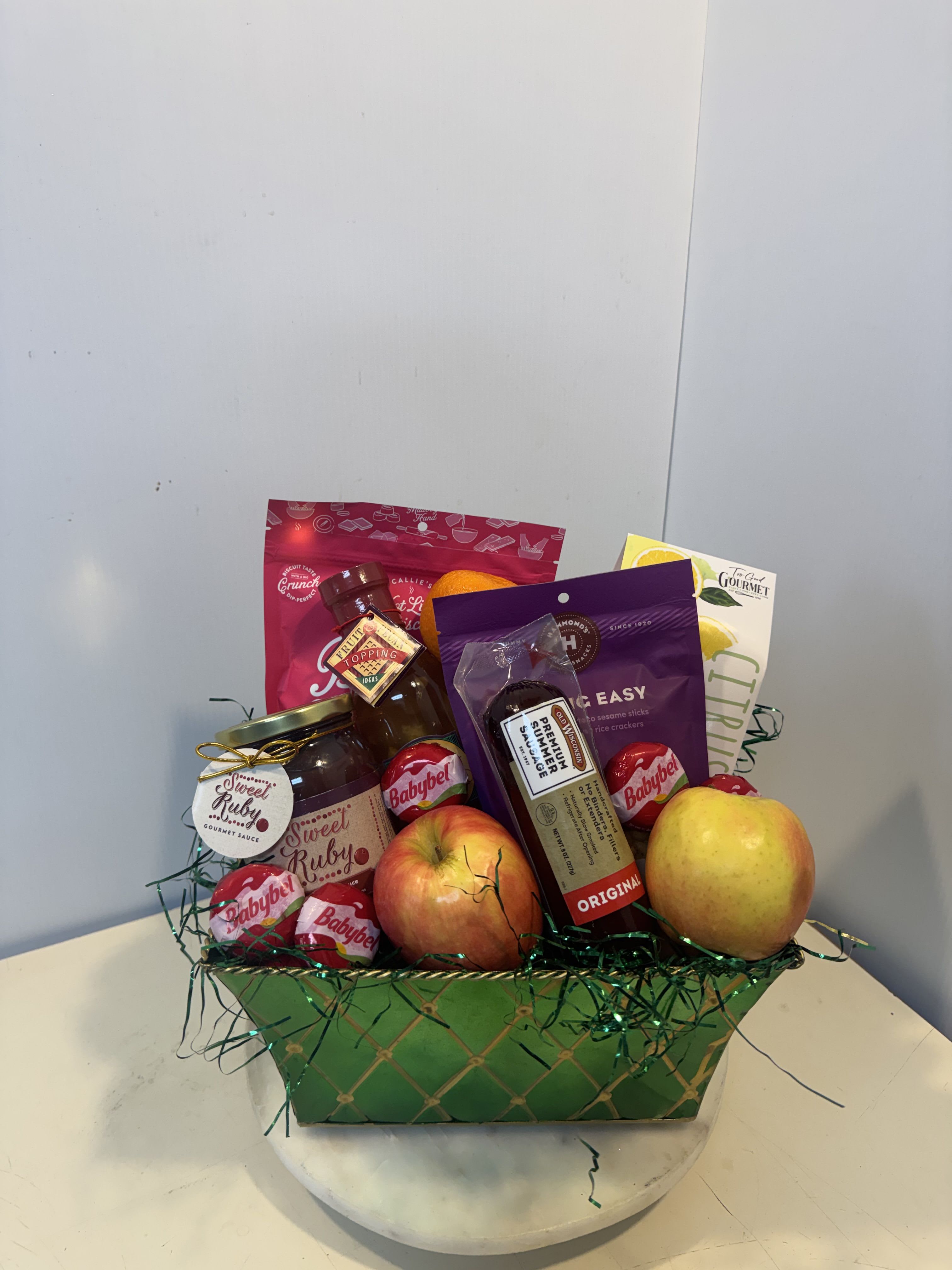 Gift basket with apples, citrus, and packaged snacks in a green container