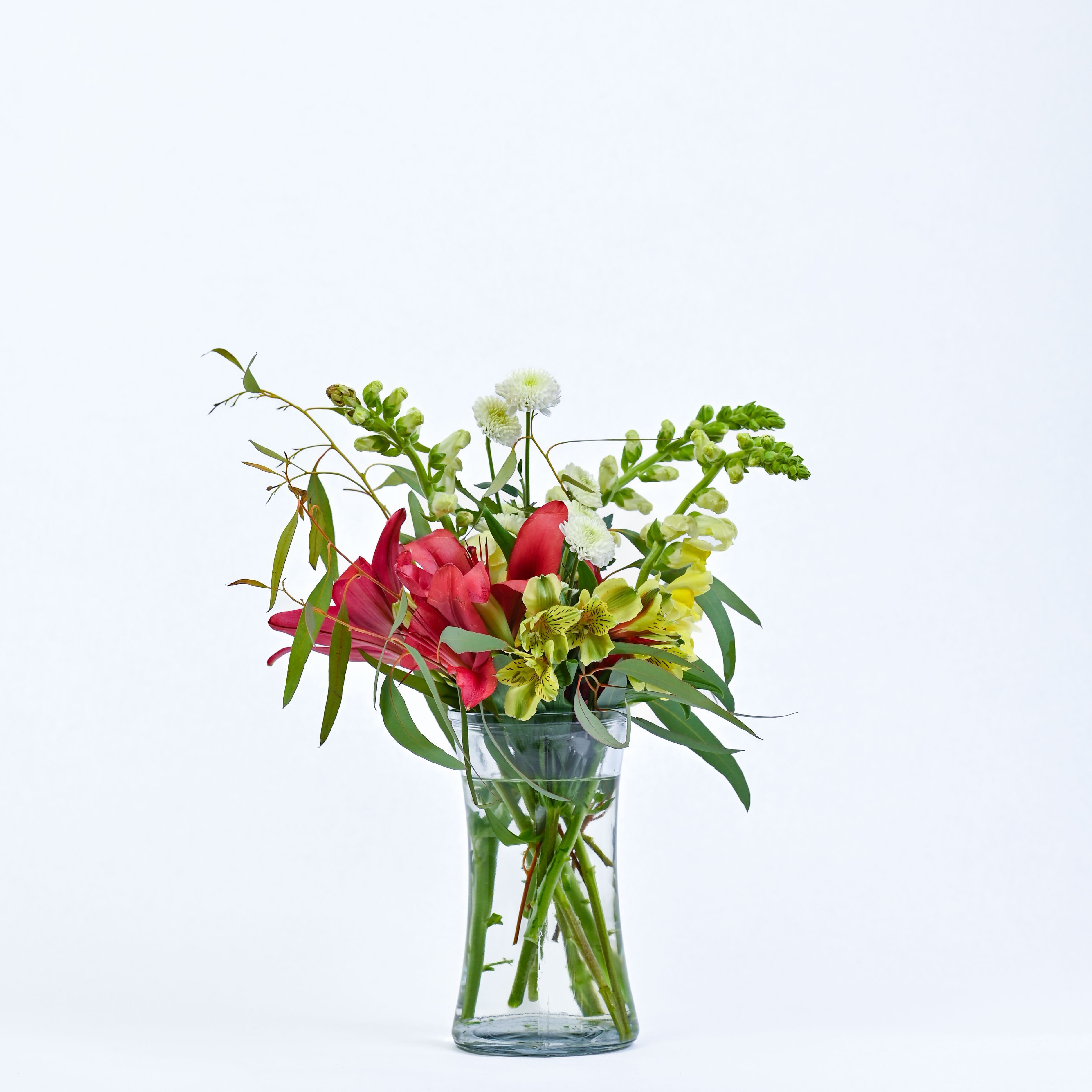 Mixed bouquet of pink lilies and green-yellow flowers in a clear glass vase