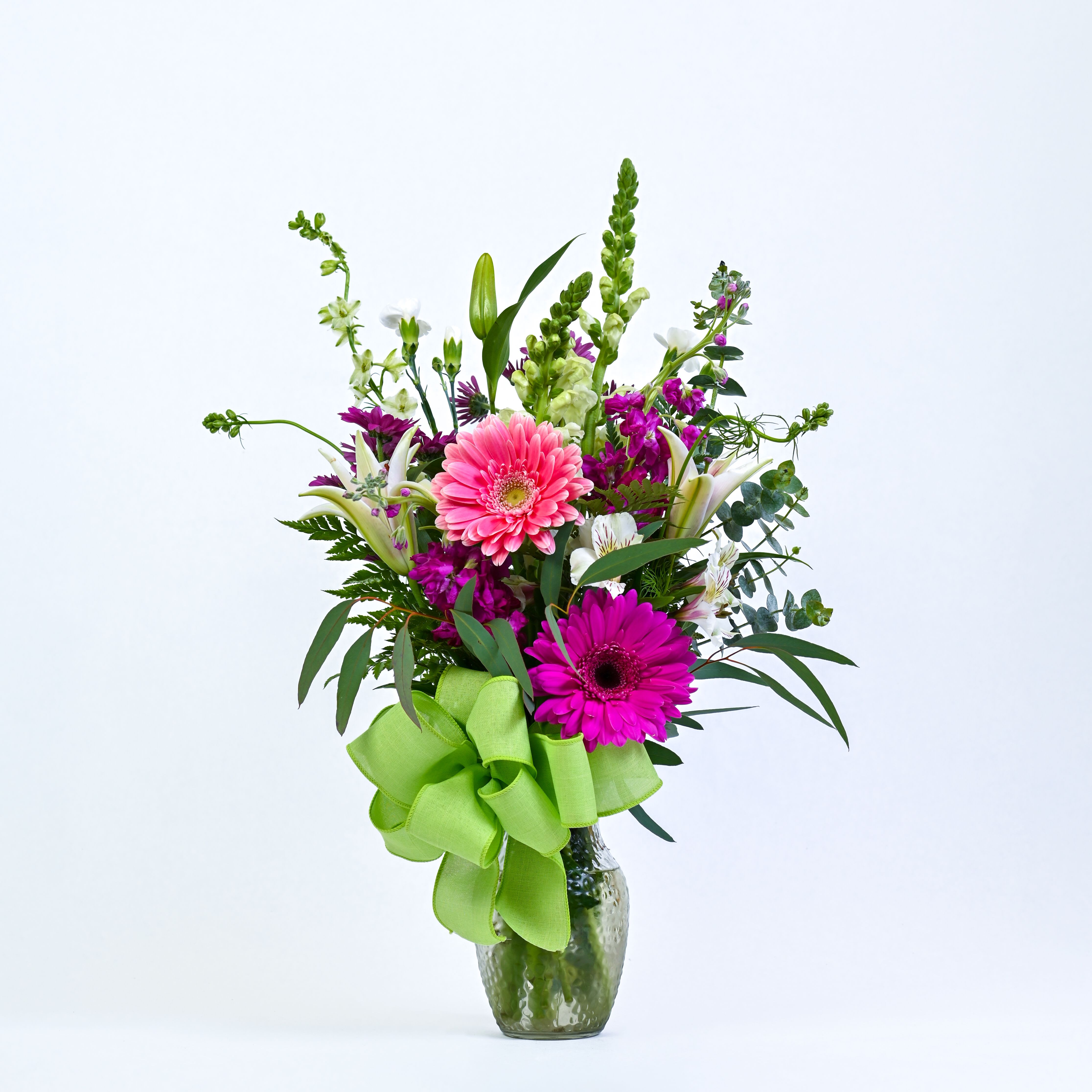 Pink and magenta gerbera bouquet in a glass vase with a green ribbon
