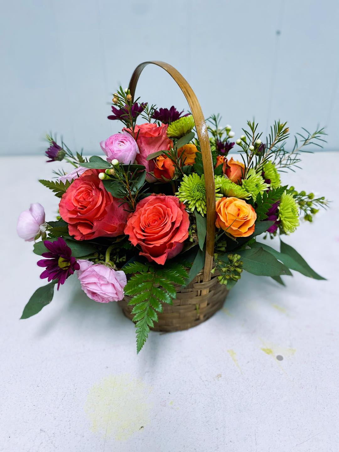 Basket of mixed roses and daisies in pink, coral, orange, and green