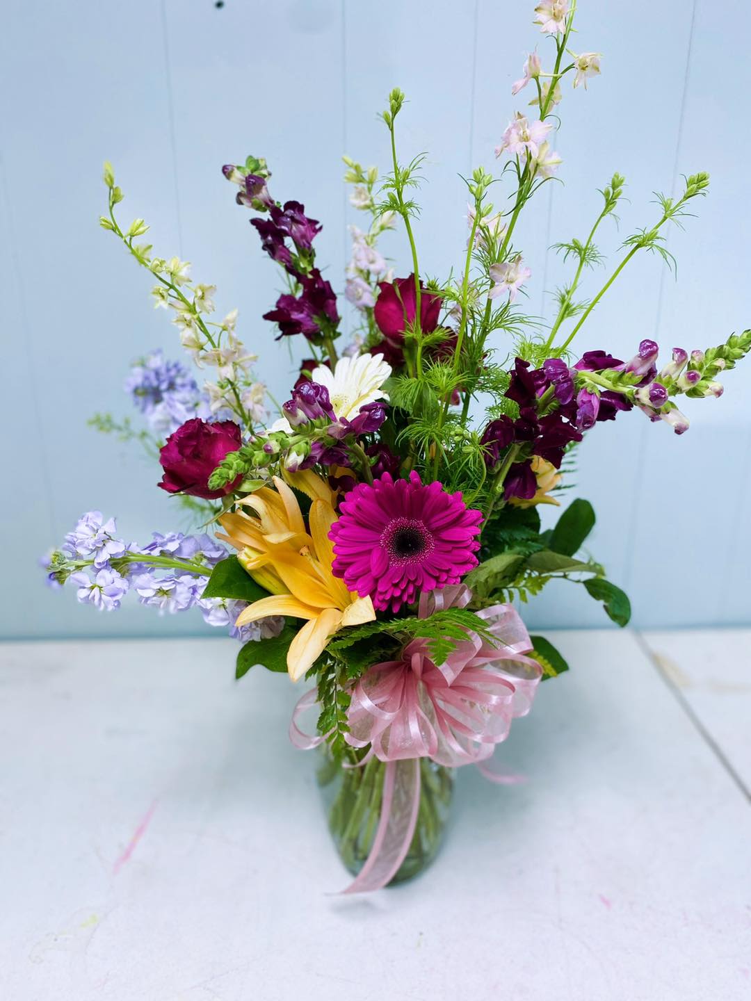 Mixed bouquet in a glass vase with pink ribbon and bright gerbera, lilies, and snapdragons