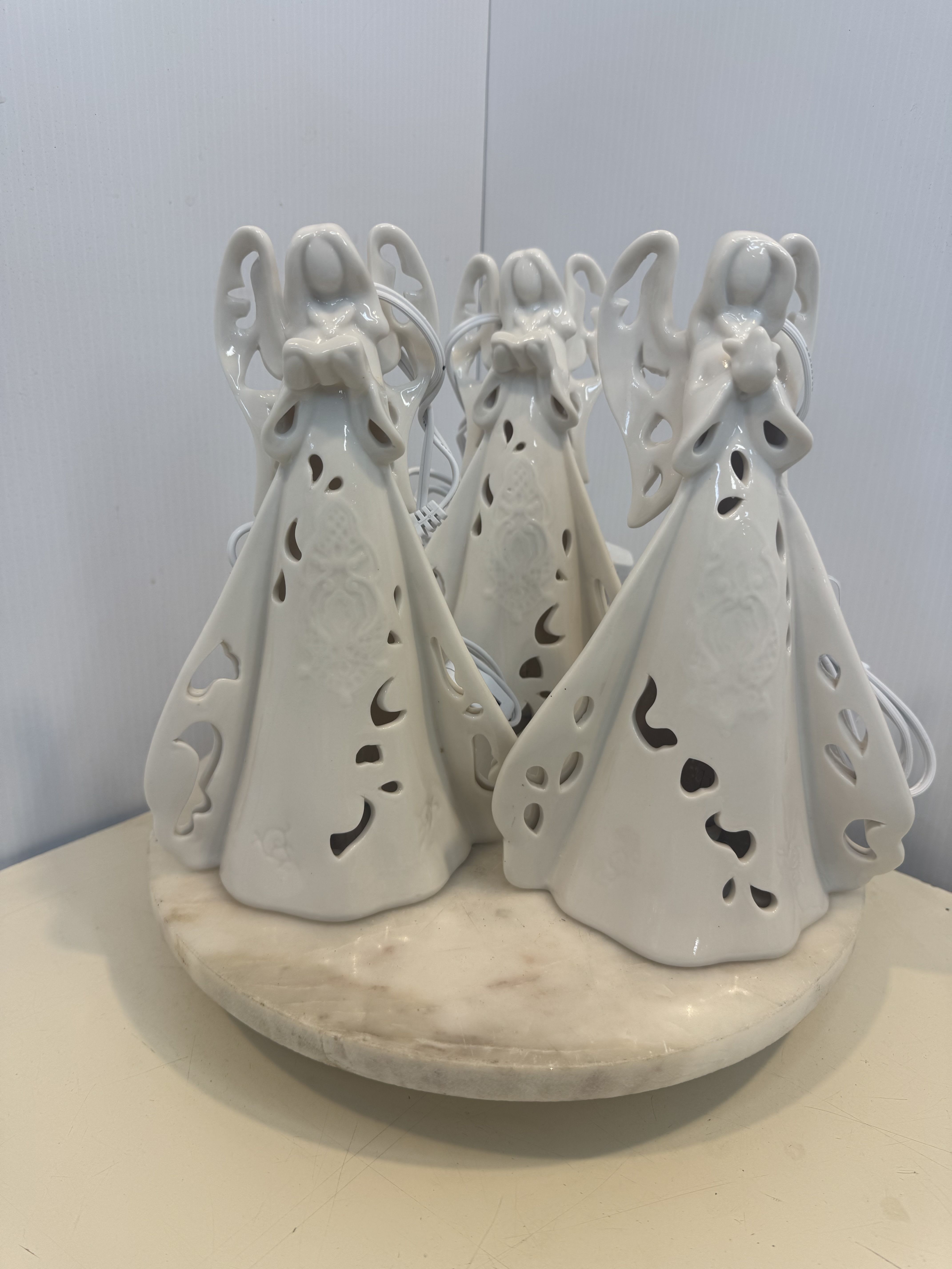 Three white ceramic angel figurines on a round base