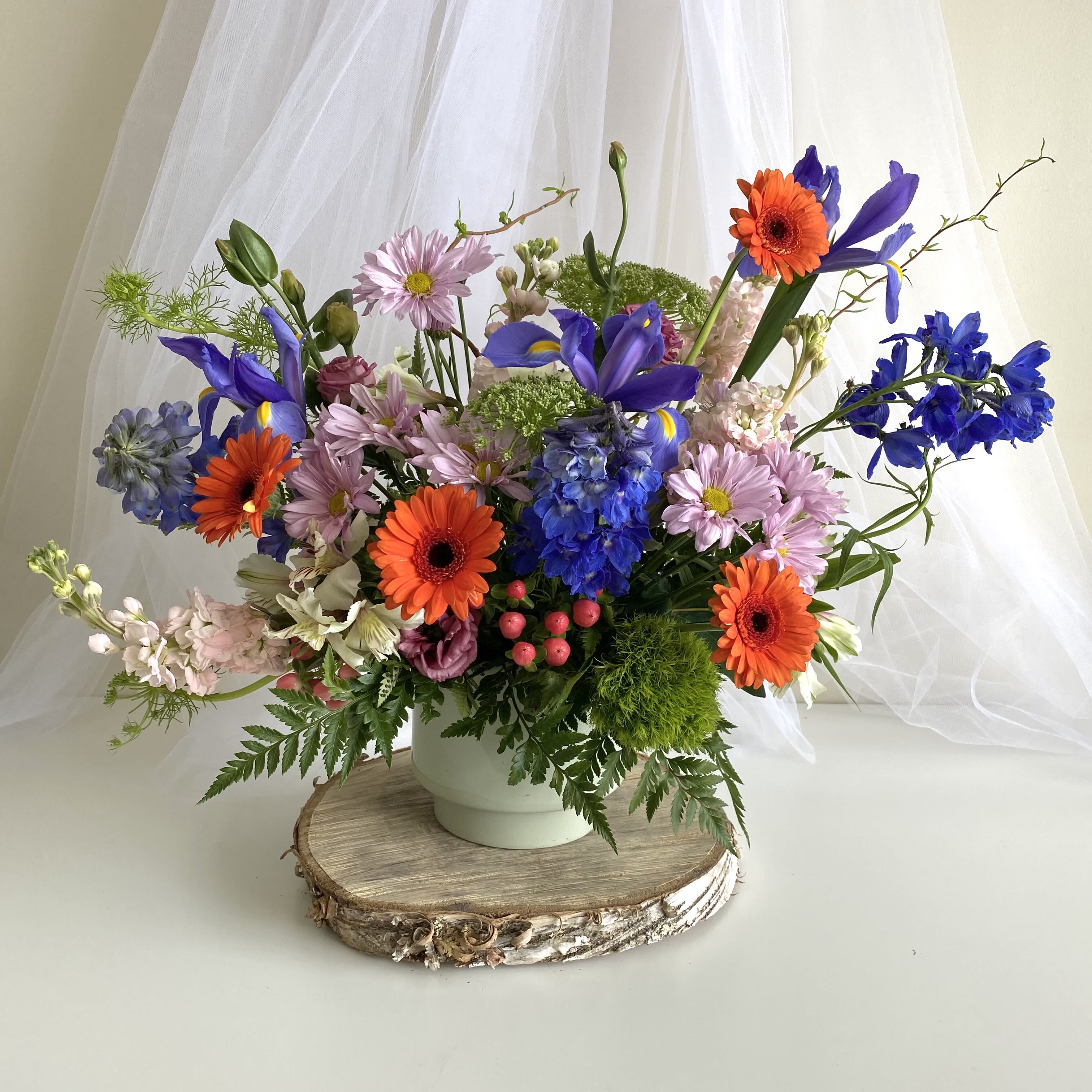 Colorful mixed flower arrangement in a white vase on a wood slice base