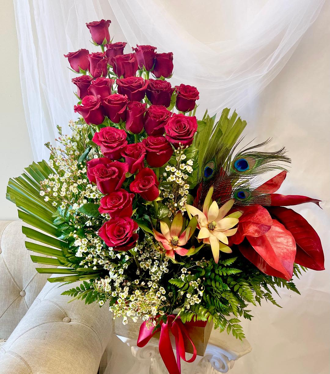 Tall bouquet of red roses with tropical accents and a red ribbon