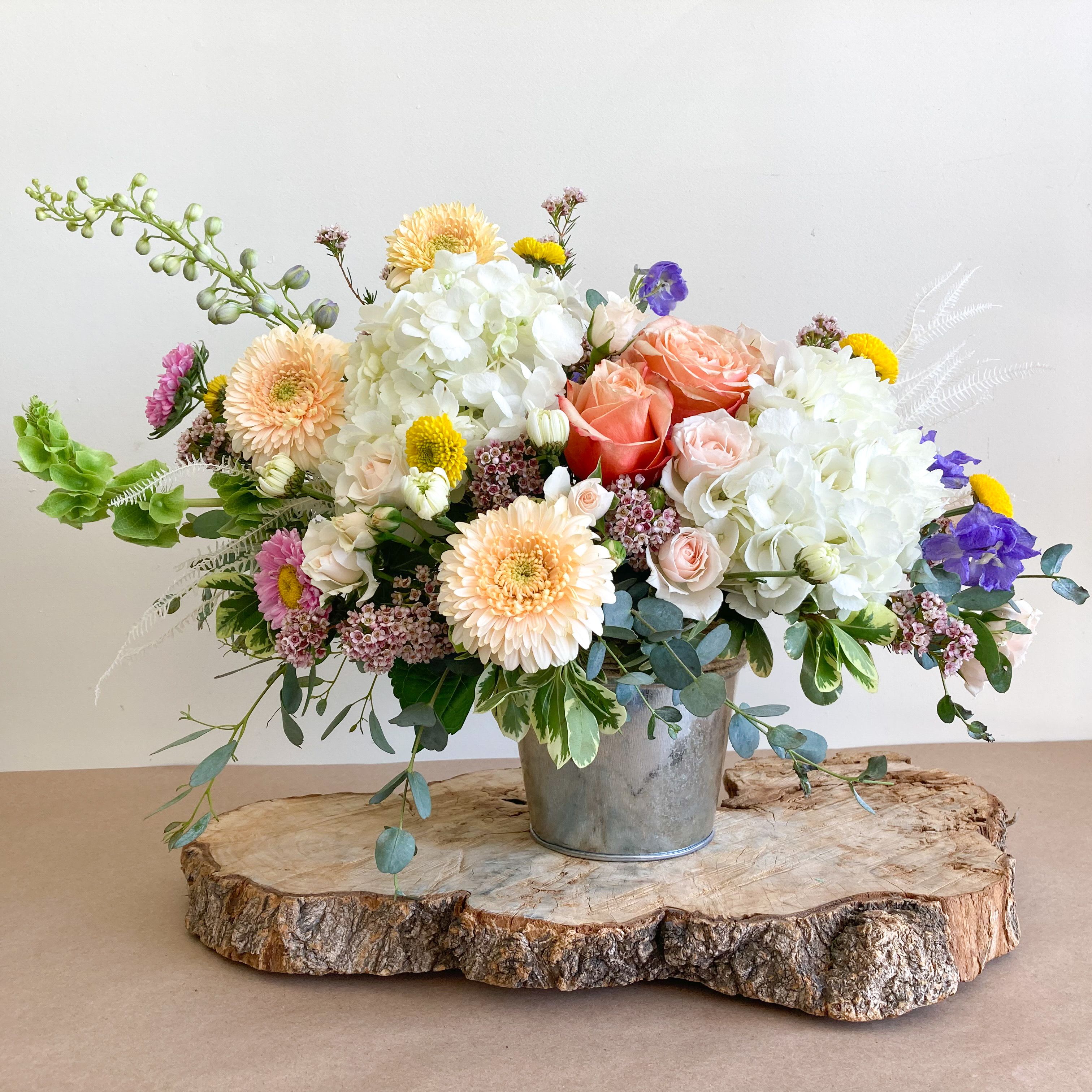 Mixed bouquet of roses, hydrangeas, and daisies in a metal bucket