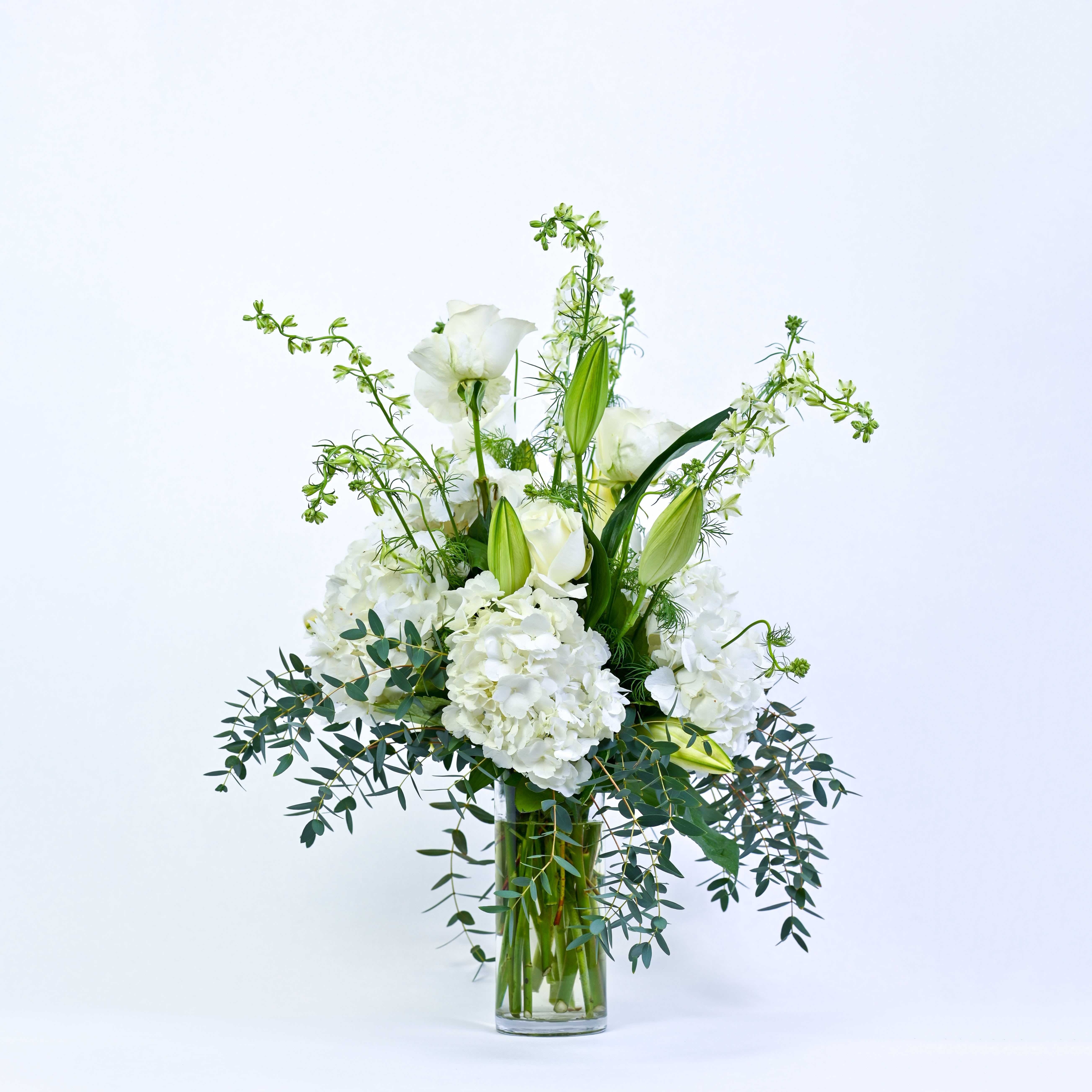 White floral arrangement in a clear glass vase with tall green accents
