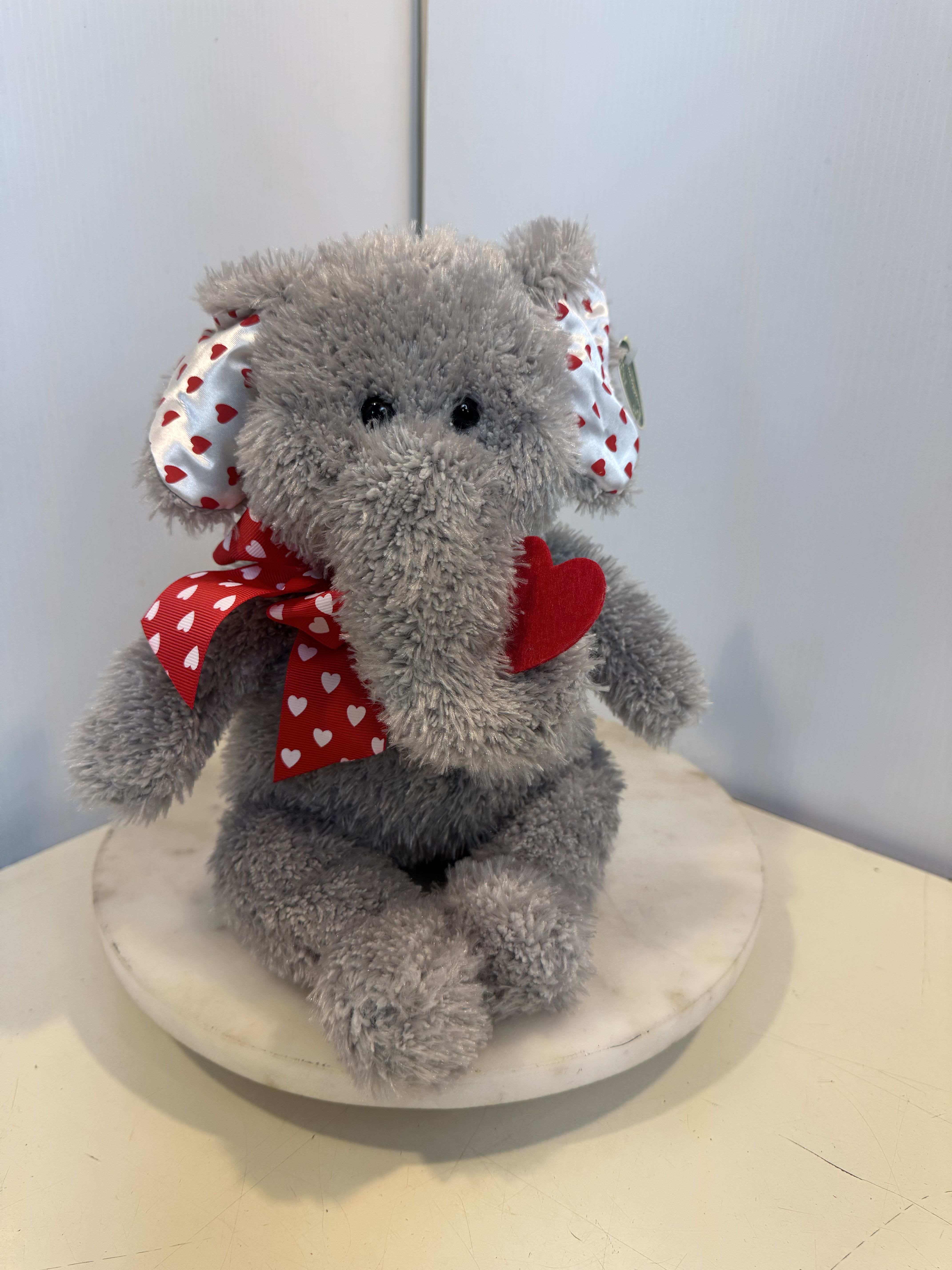 Gray plush elephant with red heart ribbon on a round base