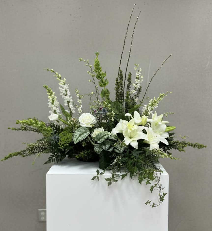 Modern English Garden - This funeral piece includes at least two houseplants for use as keepsakes and a long, sprawling base with tall garden-like blooms. A unique piece and can be customized by color or theme. 