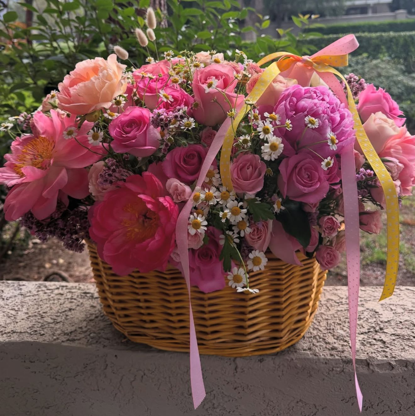 Pink and peach flowers arranged in a wicker basket with ribbon.