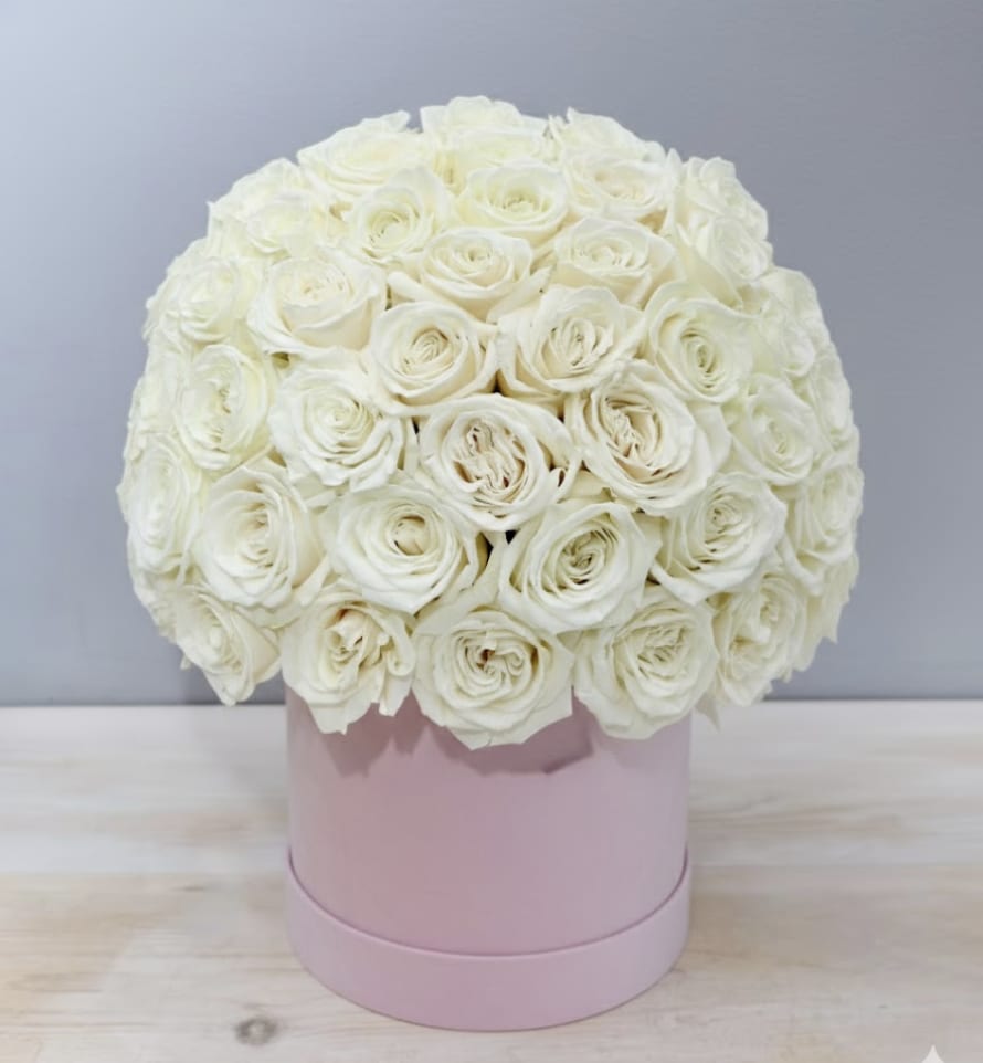 Round arrangement of ivory roses tightly packed in a pale pink hat box on a light table