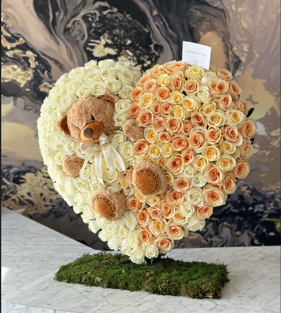 Heart-shaped rose arrangement with two teddy bears on a moss base