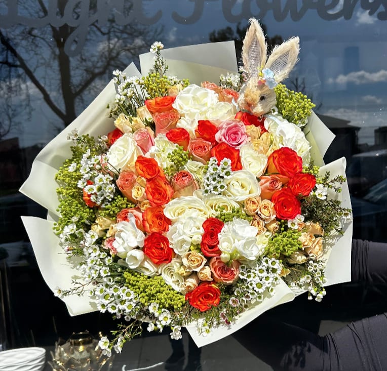 Large bouquet of red, white, and peach roses with a small bunny topper