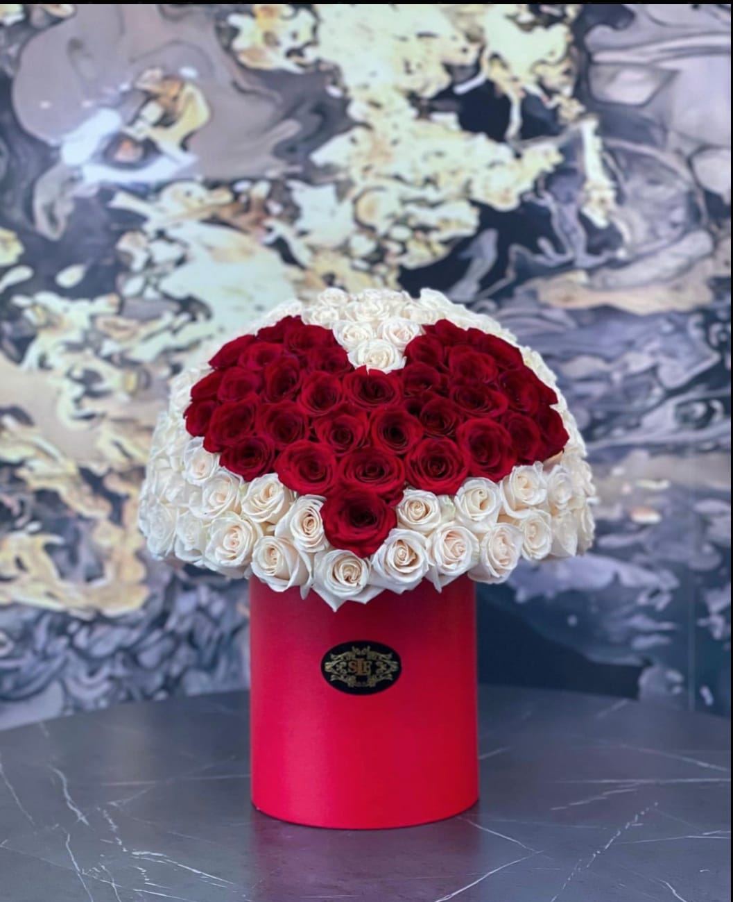 Heart-shaped red and white rose arrangement in a red cylindrical box