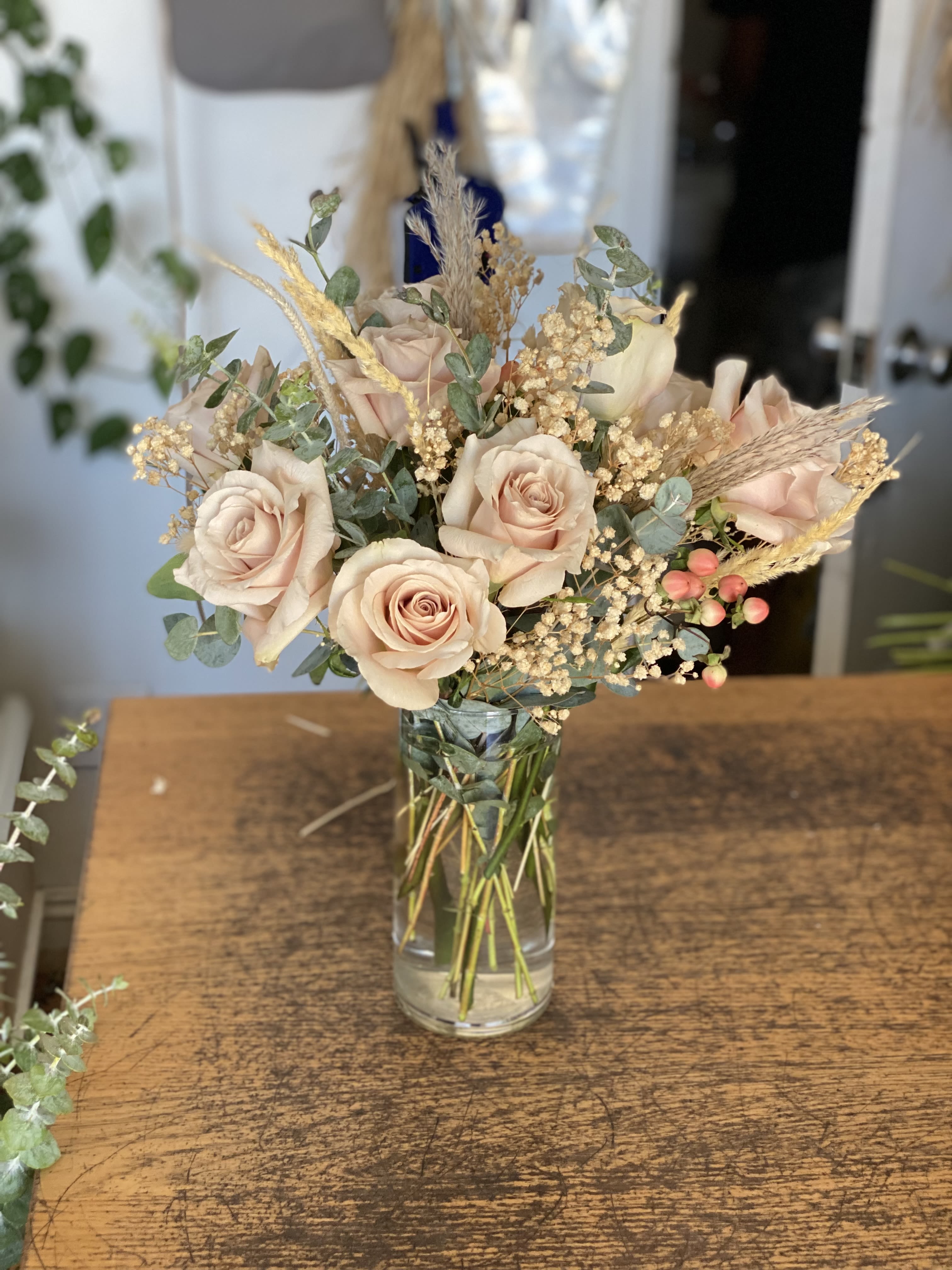 Blush roses arranged in a clear glass vase with dried grasses and filler flowers.