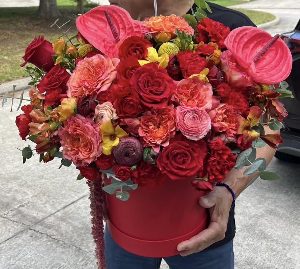 Large red and pink flower arrangement in a red hatbox with anthuriums and roses