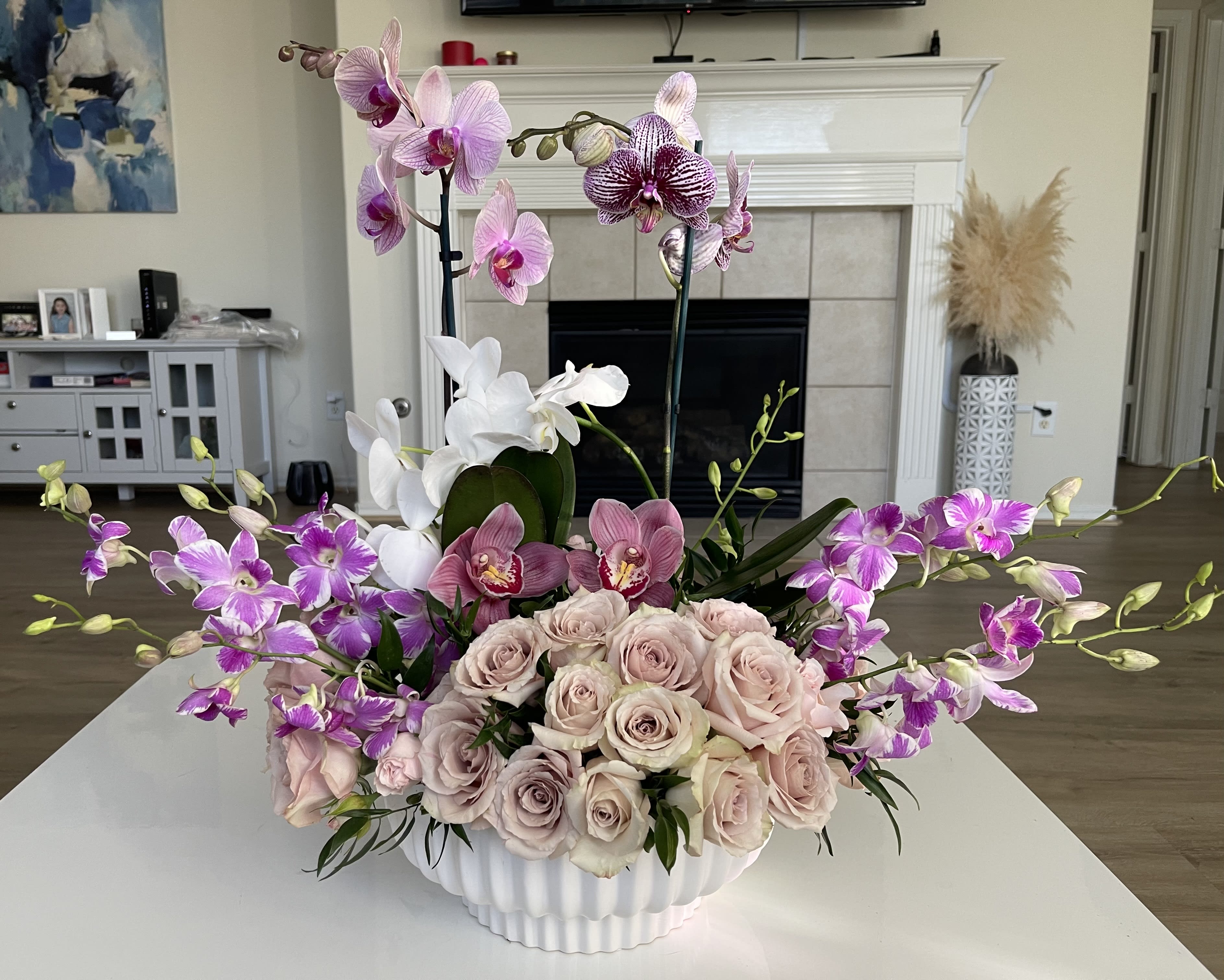 Pink and purple orchids with pale roses in a white vase