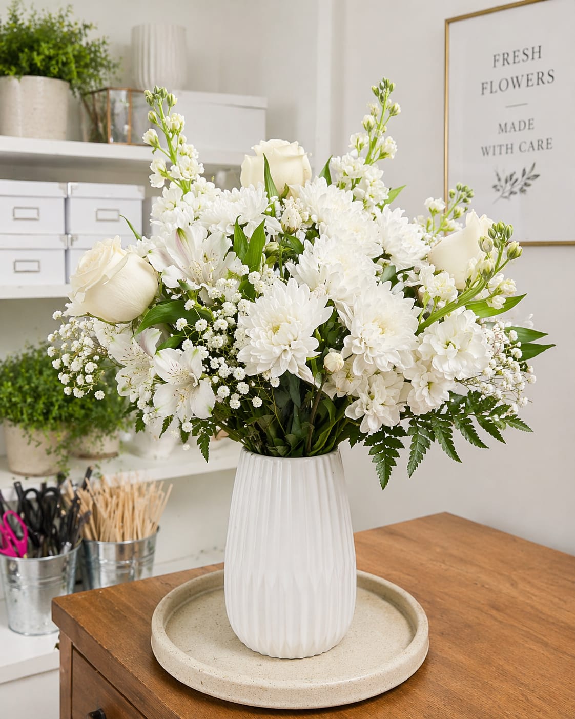Pure serenity  - A timeless all-white arrangement featuring white roses, chrysanthemums, stock, and delicate baby’s breath, styled in a modern ceramic vase. Perfect for sympathy, elegance, or a clean, sophisticated gift.