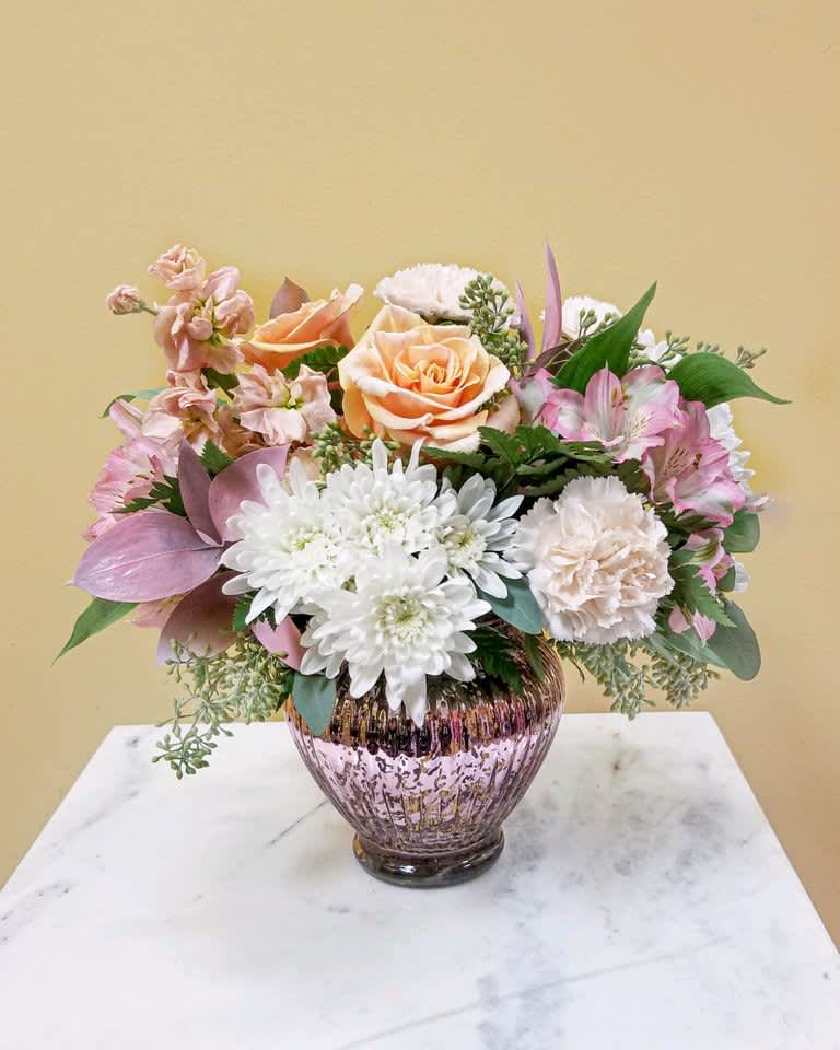Mixed bouquet of peach, pink, and white flowers in a pink glass vase
