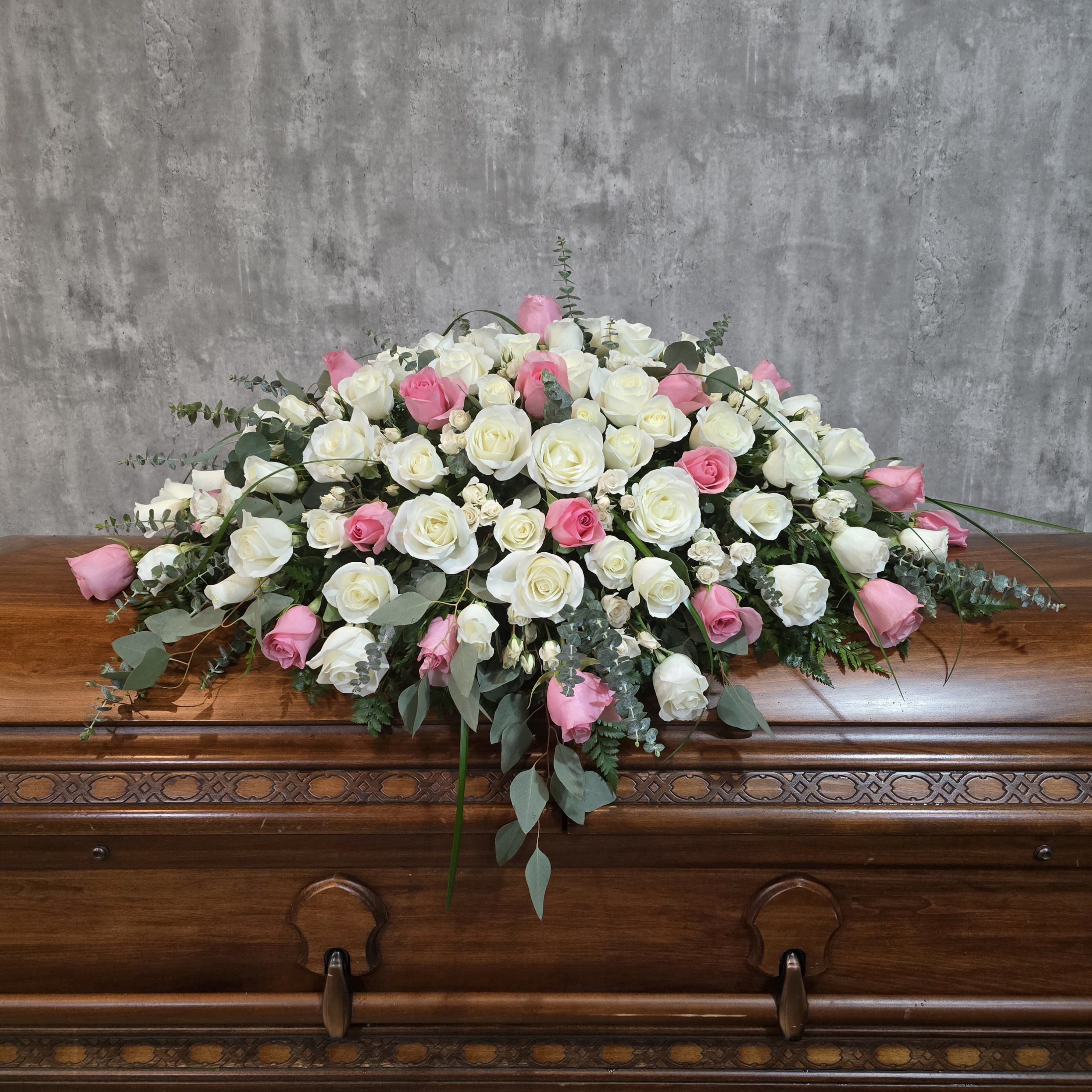 White and pink rose casket spray on a wooden casket