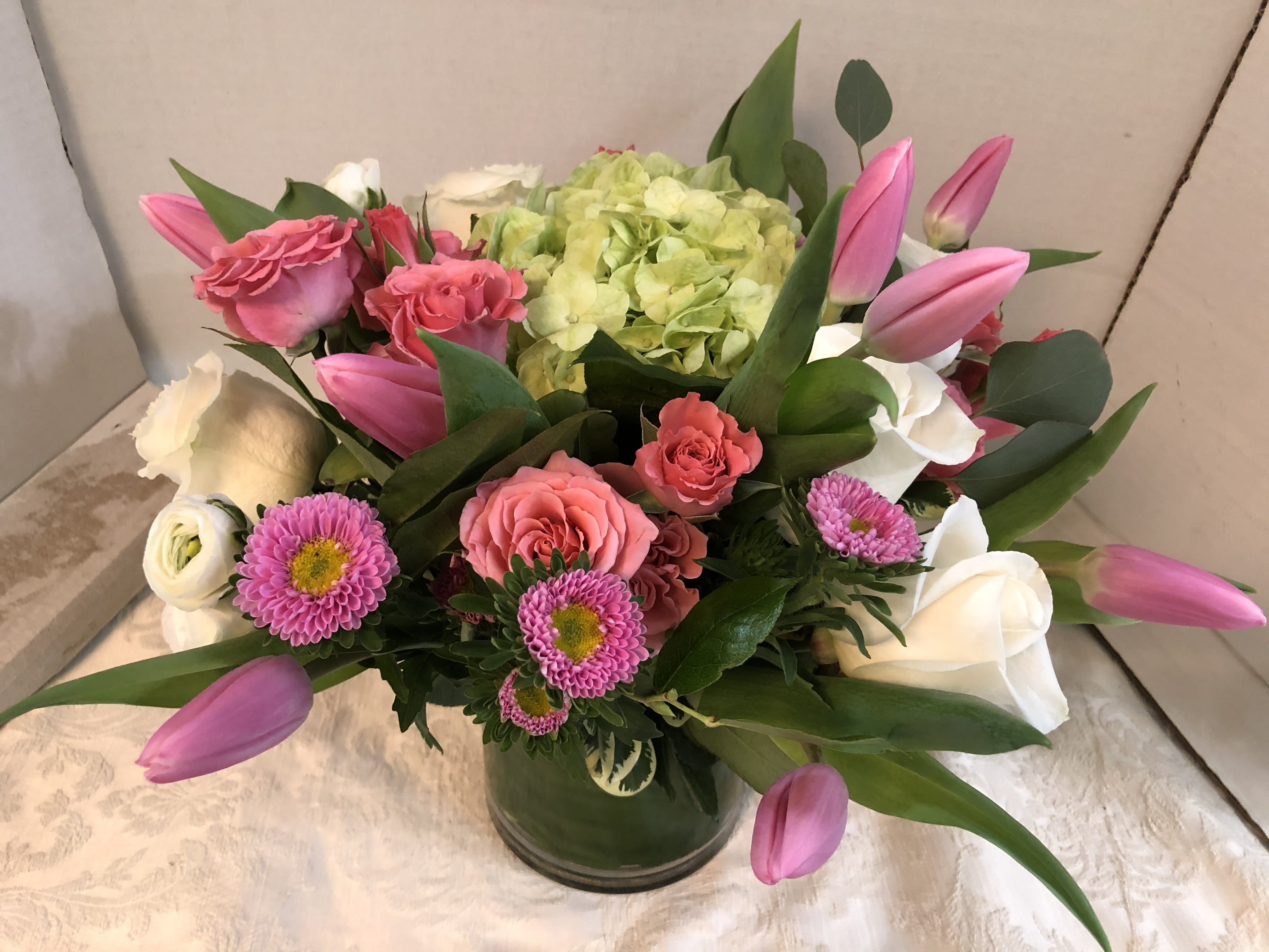 Pink tulips, roses, and white blooms arranged in a glass vase