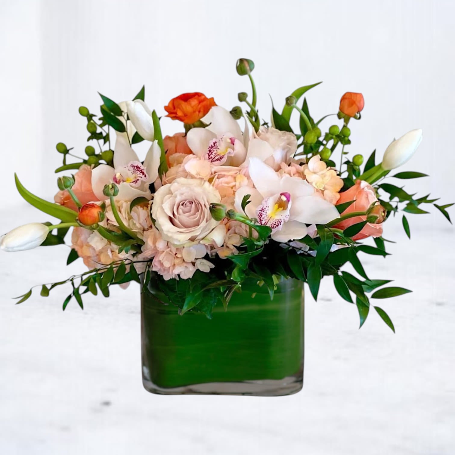 Low peach and white arrangement with roses, orchids, and tulips in a green-lined square glass vase