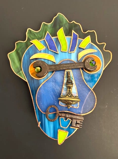 #A079 - Lizard Man - A playful mixed-media wall arrangement that reads like a bright, abstract portrait - perfect as a birthday alternative or a one-of-a-kind housewarming gift. This steampunk style art piece blends stained-glass in bold blues with lively accents of green, yellow, and orange to create hair and facial contours, delivering vivid visual impact the person you're gifting will notice the moment it's hung. The design pairs colorful glass panels with vintage metal hardware for texture and character: a dark metal wrench or horizontal key forms the upper face as stylized eyes, brass door knocker and ornate metal pieces create a prominent nose, and old-fashioned keys shape the mouth and chin. Decorative glass gems set into the metal add sparkle and depth, while copper-toned outlines hold the composition together-an eclectic mix of smooth glass sheen and aged metal patina. Made to be displayed on a wall, this whimsical piece suits anyone who loves artistic, handmade-style decor and unexpected conversation starters. It's ideal for creative living rooms, studios, or entryways and arrives ready to hang; its durable materials require only occasional dusting to keep the colors bright.  Shipping available - select Delivery, then message us to ship.