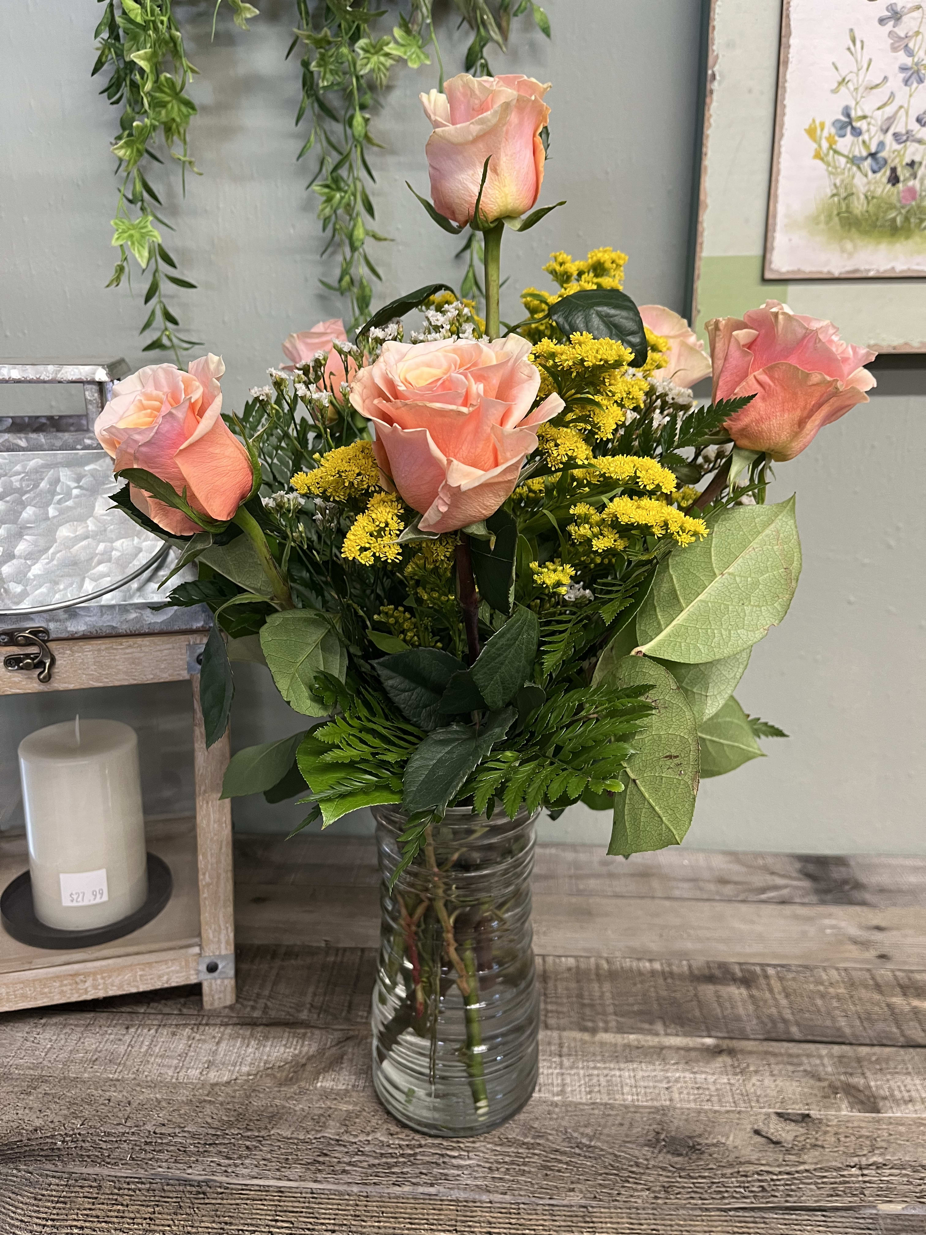 Pink roses arranged in a clear glass vase with yellow filler flowers