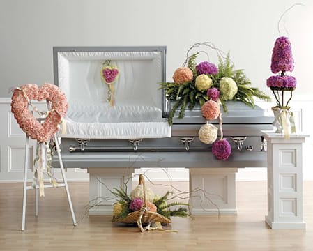 Casket surrounded by pastel floral arrangements and a heart-shaped wreath