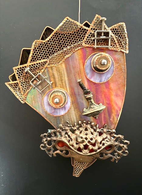 #A122 - "Mustached Man" Mask - A playful industrial portrait that doubles as wall art, this mixed media wall sculpture presented as a mustached metal mask is a standout piece for housewarming gifts, eclectic home décor, or anyone who loves steampunk inspired design. The shield shaped face glows with iridescent, rainbow banded metal that catches light, while the mask motif and bold color accents (orange, black, purple, pink, and mixed hues) create an instantly memorable visual that will make the person you're thinking of smile and spar with delight.   Layered metal gears, buckles, circular fittings and small hardware elements form expressive eyes and a sculptural nose; ornate bronze toned filigree shapes the textured mustache and mouth, and honeycomb style metal mesh rises like a jagged crown for stylized hair. Stained glass panels and metal decorative filigree add warmth and depth, and the combination of copper, bronze and iridescent finishes gives the piece both shimmer and tactile contrast-perfect for a creative mantle, entryway or studio wall.   Give this as a distinctive gift to mark an artist's birthday, a quirky anniversary, or to celebrate a new home-she'll feel seen by something that reflects her unique taste. The wall mask arrives ready to hang as a decorative accent; because it's crafted from metal and glass components it requires only a secure wall hook and occasional dusting to keep the finishes bright.  Shipping available - select Delivery, then message us to ship.