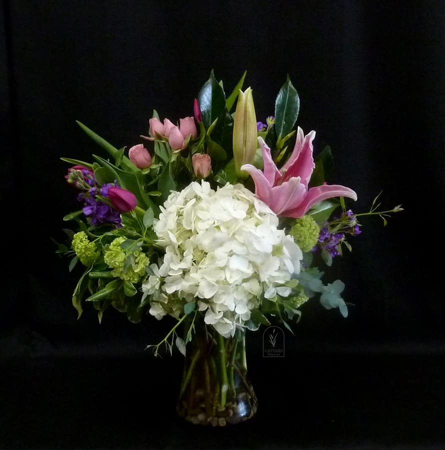 Southern Belle - Southern Belle is a charming, graceful arrangement that captures timeless elegance with a soft, romantic touch. Featuring lush white hydrangea, fragrant pink lilies, delicate spray roses &amp; tulips, and vibrant seasonal accents, it’s artfully gathered with fresh greenery in a classic glass vase. Sweet, refined, and effortlessly beautiful, this design brings a hint of Southern charm to any space.
