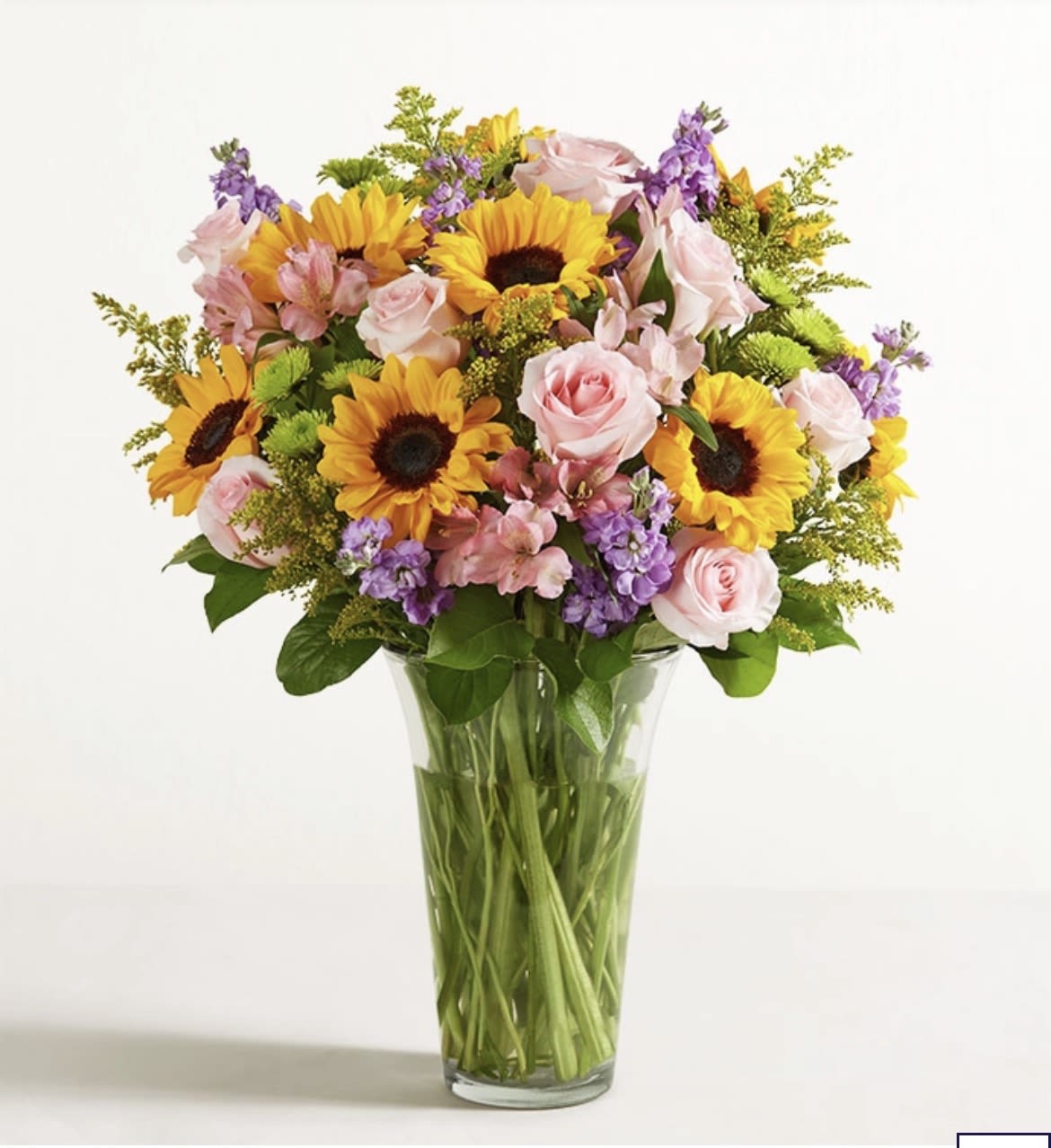 Bouquet of sunflowers, pink roses, and purple flowers in a clear glass vase