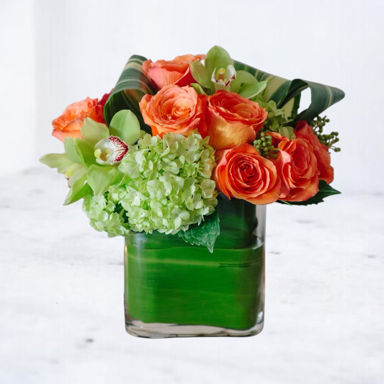 Citrus Radiance - Add a vibrant splash of joy to any room with Citrus Radiance, a bold and modern flower arrangement designed to energize the senses. Featuring vivid orange roses, lush green hydrangeas, and striking green cymbidium orchids, this eye-catching bouquet is a celebration of color, texture, and contemporary style.  Perfect for birthday flowers, congratulatory gifts, thank-you surprises, or simply brightening someone’s day, Citrus Radiance makes a stunning statement for any occasion. Arranged in a sleek glass vase, it's a show-stopping piece that brings life and cheer wherever it’s placed. 