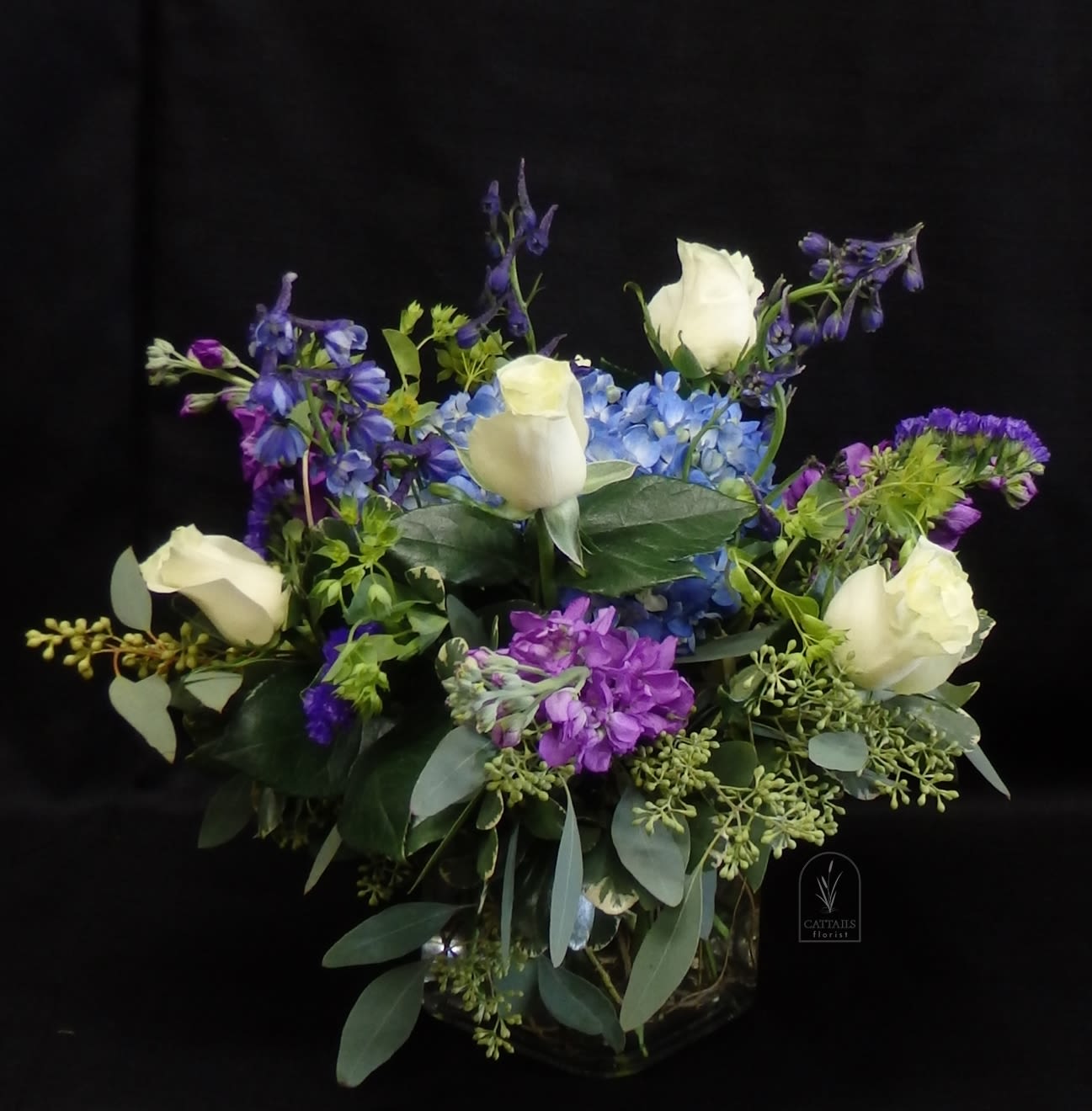 Cool Comfort - Graceful and soothing, "Cool Comfort" blends soft white roses, vibrant blue delphinium, and delicate hydrangea with accents of lavender stock and fresh greenery. Arranged in a clear glass vase, this serene mix offers a gentle expression of sympathy, support, or quiet celebration—perfect for moments that call for peace and heartfelt beauty. 