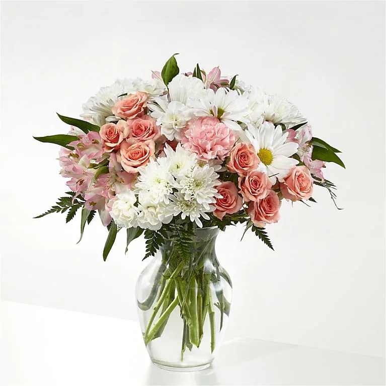 Blush Atelier - Soft blush roses gather with bright white daisy-like blooms to create an airy, rounded flower arrangement perfect for a birthday bouquet, anniversary flowers, or a heartfelt thinking-of-you gift. The mix of pale pink alstroemeria and pink carnations frames the white center, giving the person you're sending it to a warm, romantic yet relaxed impression-the kind of bouquet that makes someone feel genuinely seen.  This full, balanced arrangement is presented in a clear glass vase so stems are visible and the composition reads classic and fresh. The palette of white, pink, and green combines varied textures-velvety roses, delicate daisy petals, striped alstroemeria, and soft carnations-with fern-like foliage at the base for a light, natural finish. Sized for everyday gifting, it arrives ready to display; keep it in fresh water and trim stems occasionally to extend vase life.