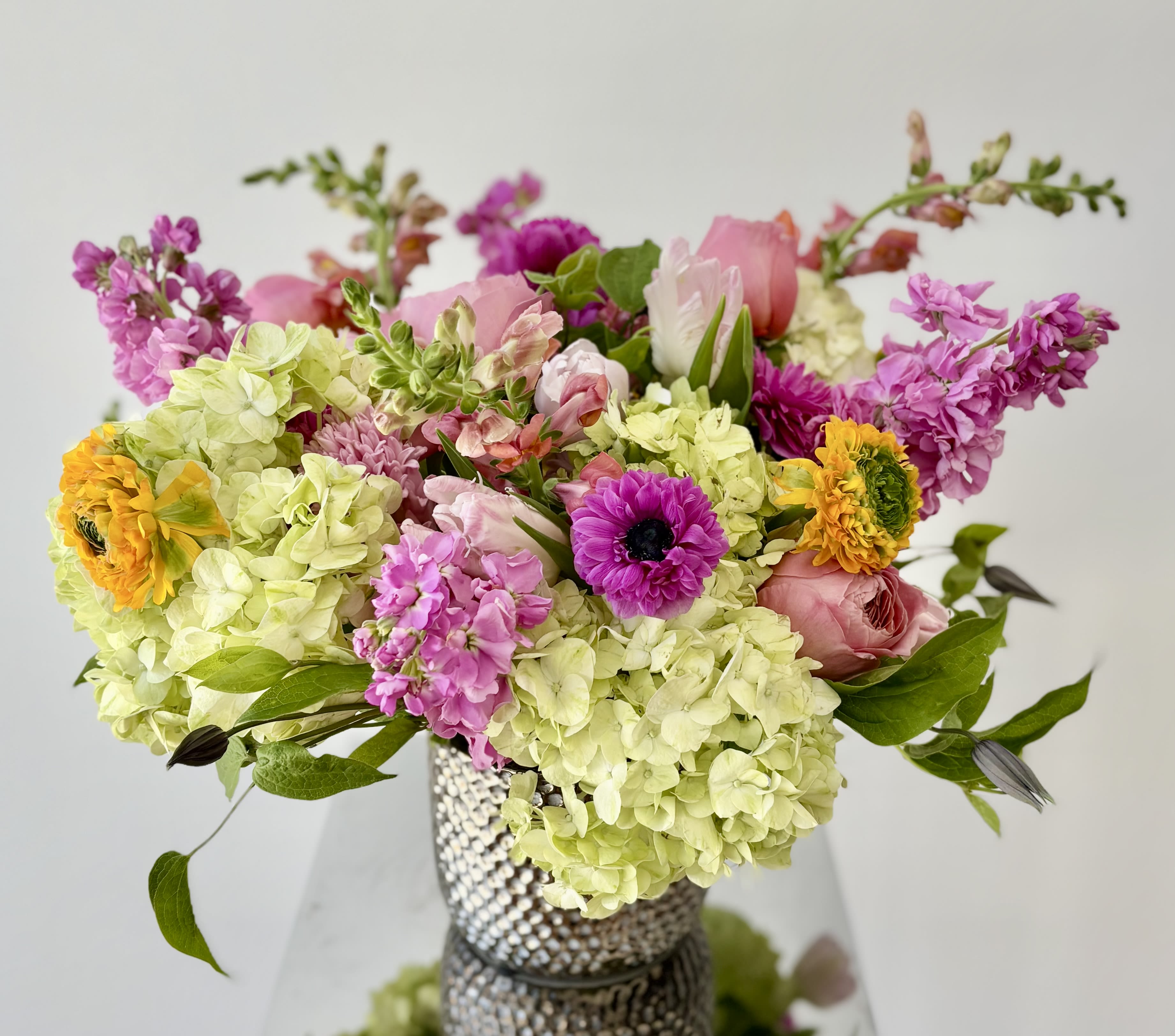 Mixed bouquet of pink, yellow, and green flowers in a textured vase