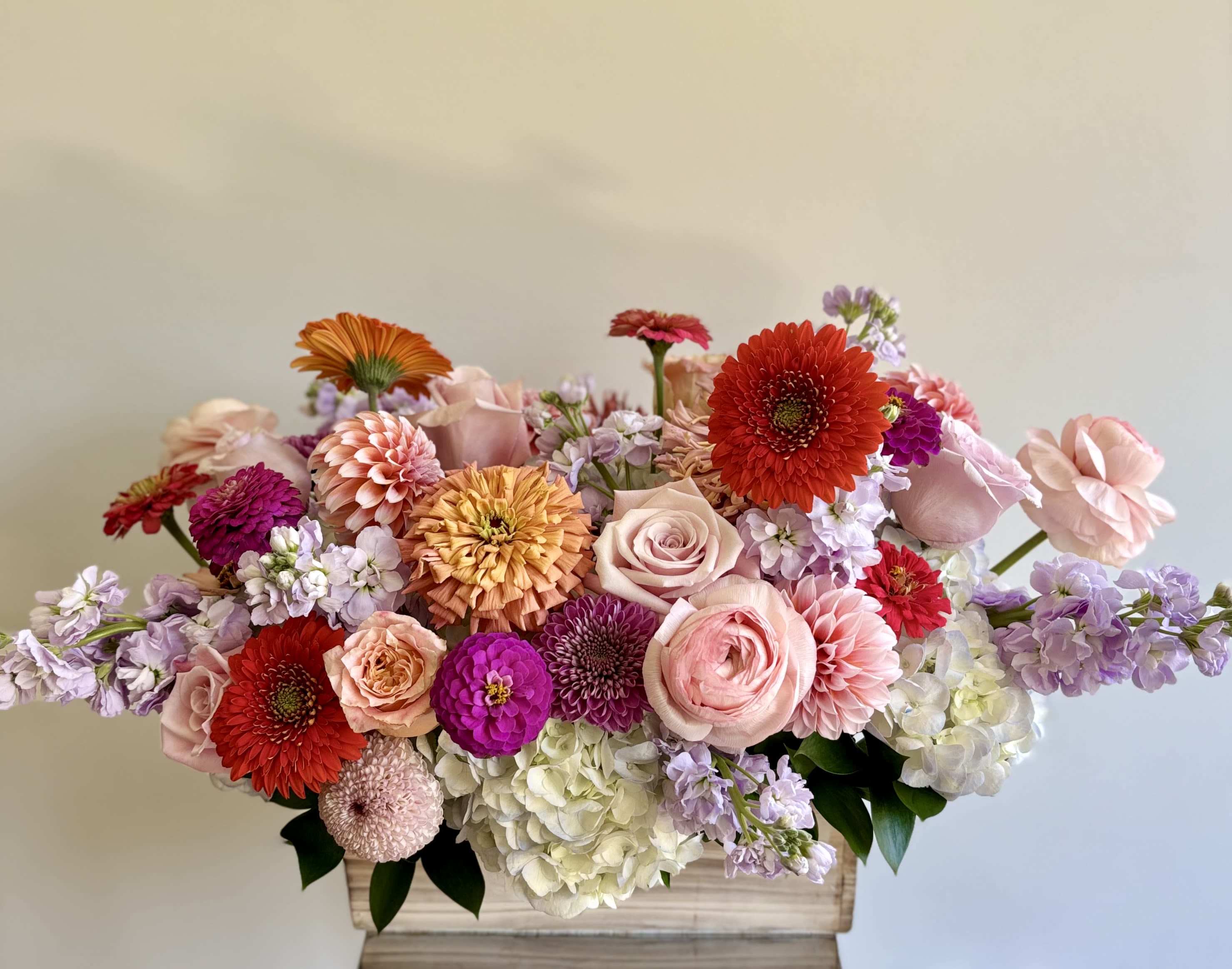 Low mixed flower arrangement in a rectangular wooden box with pink, red, and lavender blooms.